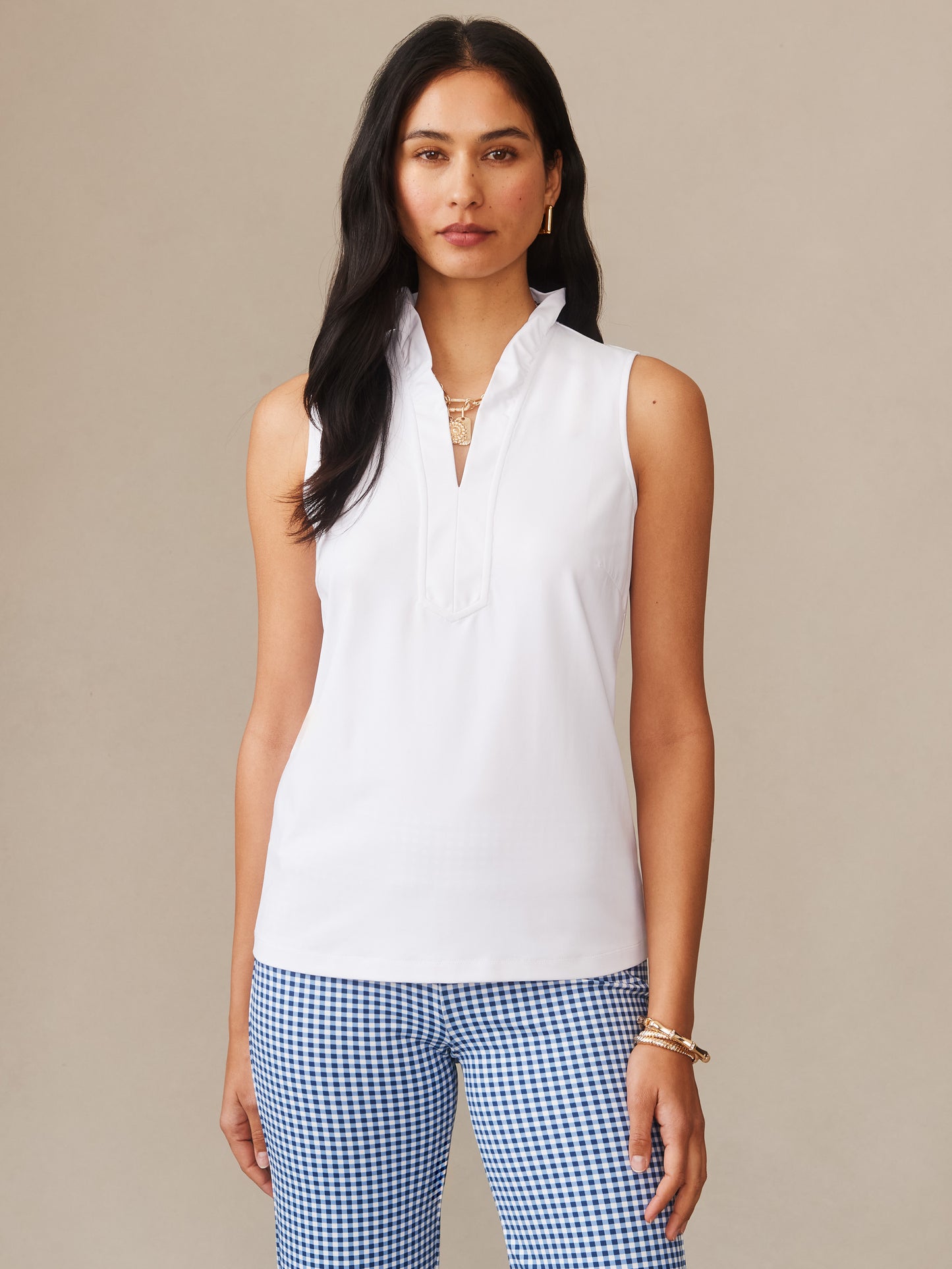 Model wearing a white Kate Sleeveless Ruffle Top from J.McLaughlin paired with blue and white gingham pants, showcasing effortlessly stylish, enduring designs in innovative fabrics.