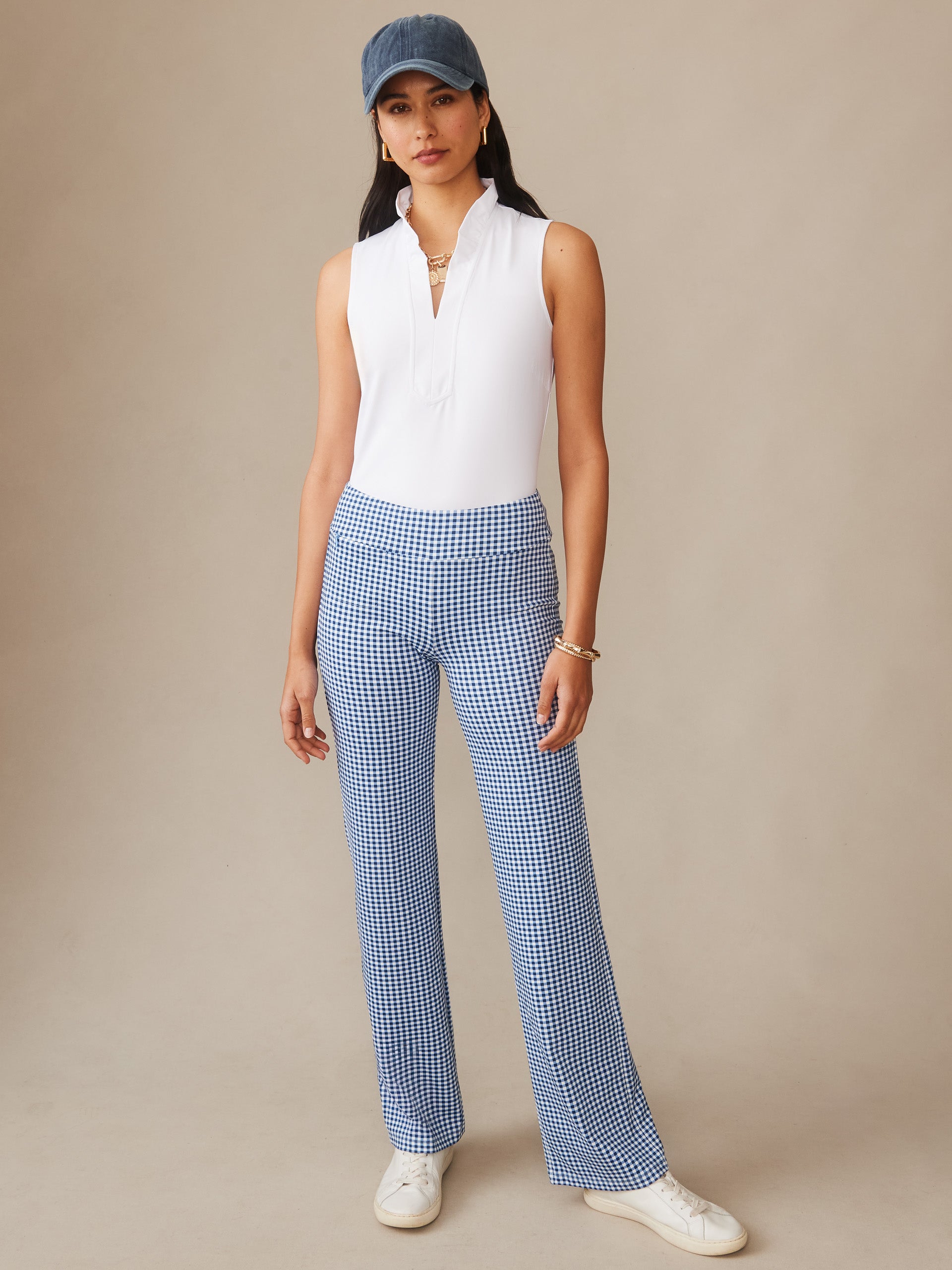Woman wearing J.McLaughlin Carmel Pants in Midi Cabana Gingham paired with a sleeveless white top and a denim cap, showcasing effortlessly stylish pants with enduring designs in a timeless look.