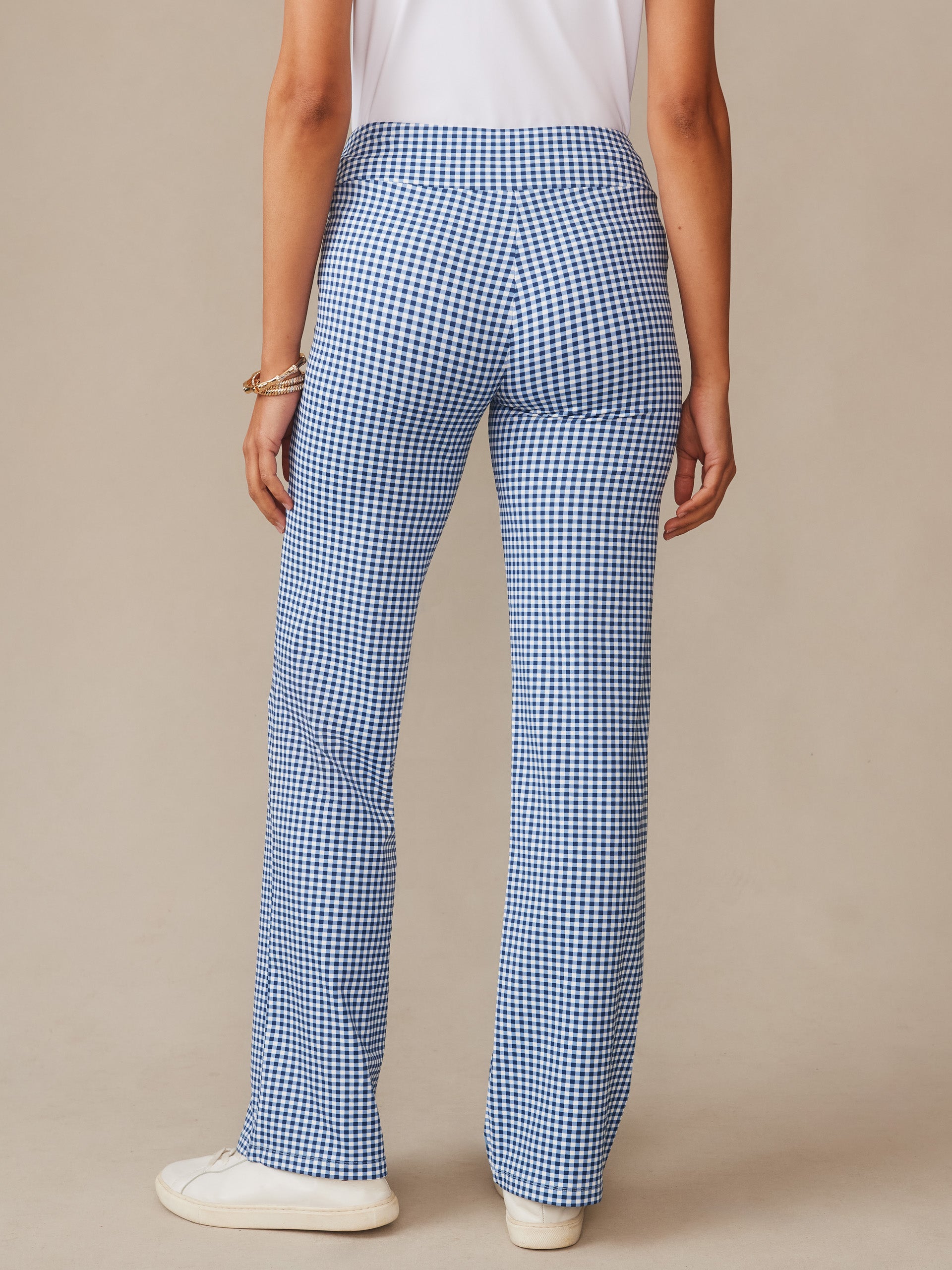 Back view of a model wearing J.McLaughlin Carmel Pants in Midi Cabana Gingham blue and white checked pants paired with a white top and sneakers, showcasing effortlessly stylish design and enduring appeal in innovative fabrics.