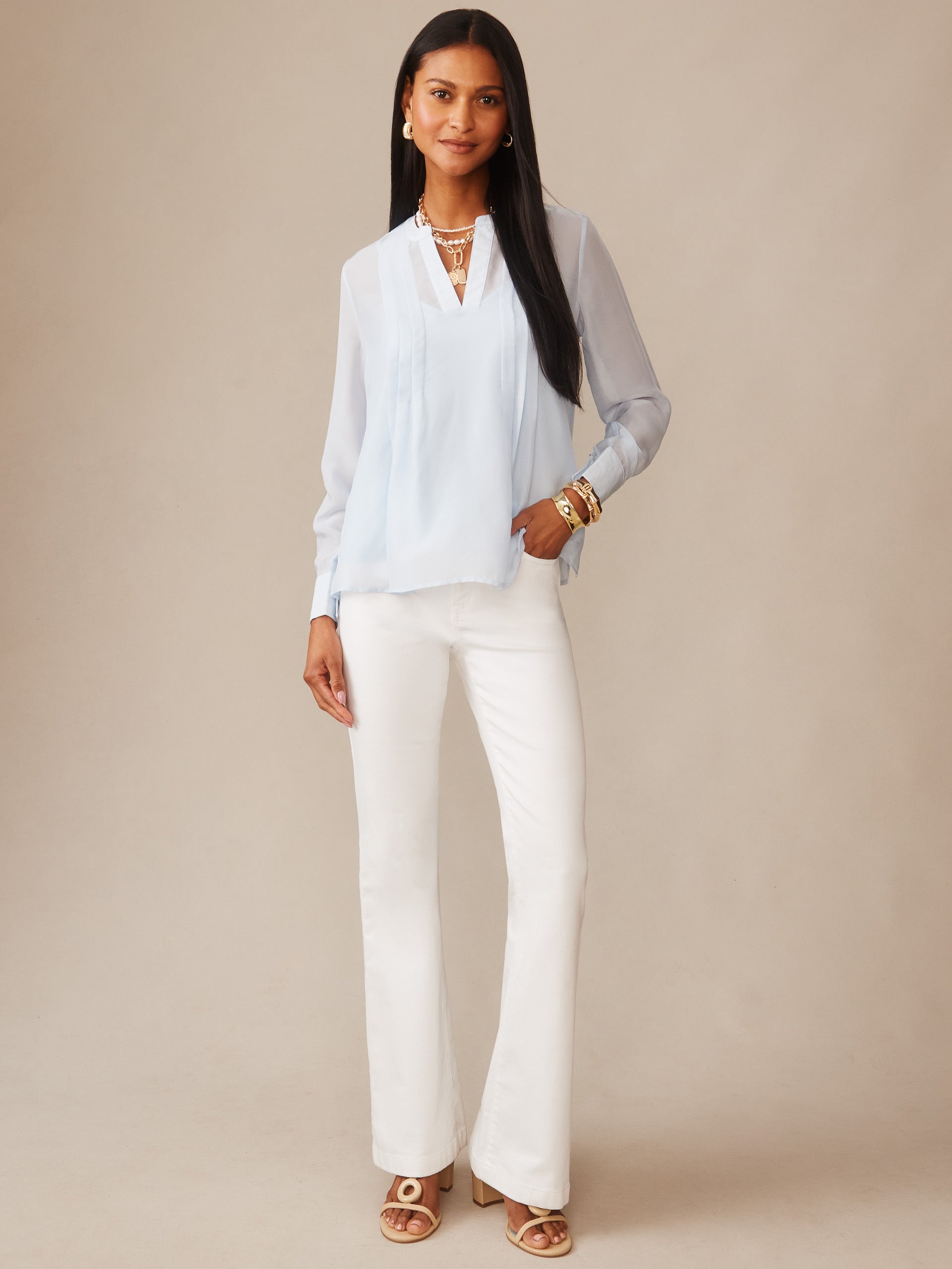 Woman wearing a light blue Katherine Silk Chiffon Blouse by J.McLaughlin paired with white pants and gold accessories, showcasing effortlessly stylish, enduring designs in innovative fabrics.