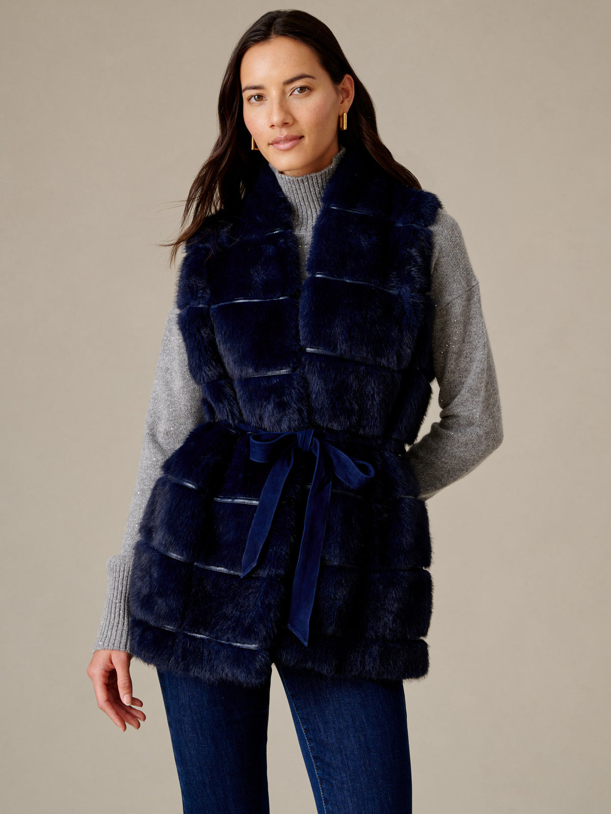 Keley Faux Fur Vest by J.McLaughlin styled on a model with plush navy faux fur panels and a suede tie belt over a gray sweater and jeans