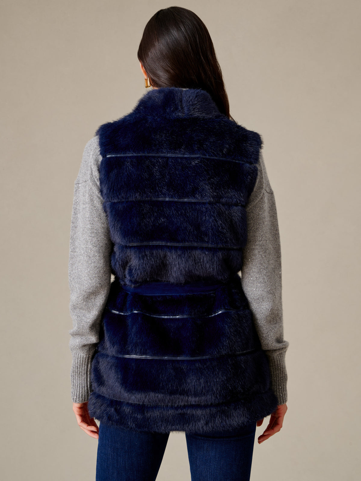 Keley Faux Fur Vest by J.McLaughlin shown from the back in navy plush faux fur with a suede tie belt layered over a gray sweater and jeans