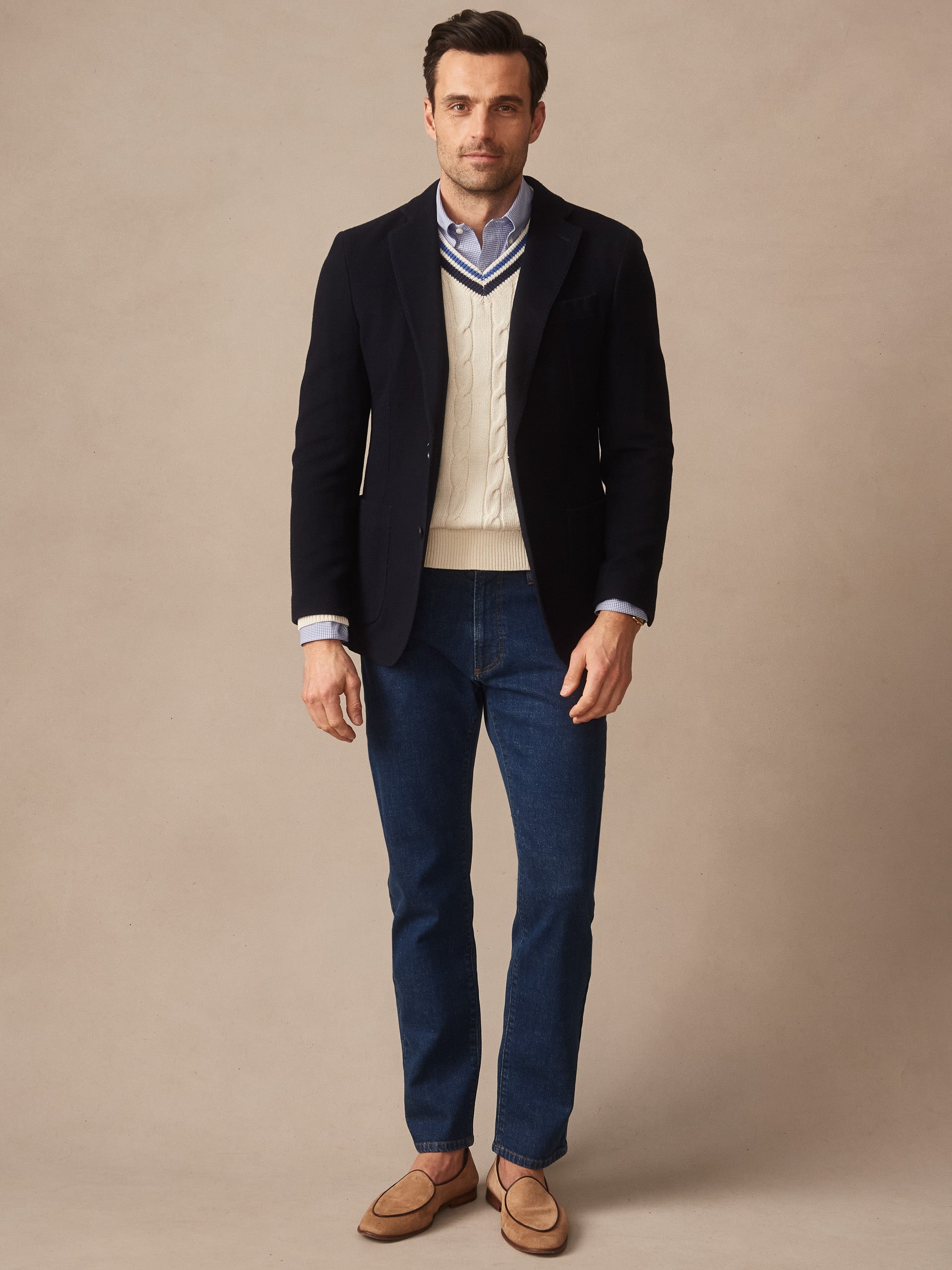 Man wearing a smart casual outfit featuring the Canary Knit Blazer by J.McLaughlin over a white cable knit vest and blue shirt, paired with dark jeans and tan loafers, showcasing effortlessly stylish, enduring designs with a legacy of timeless fashion. A destination for defining style. Life, Well-Lived.