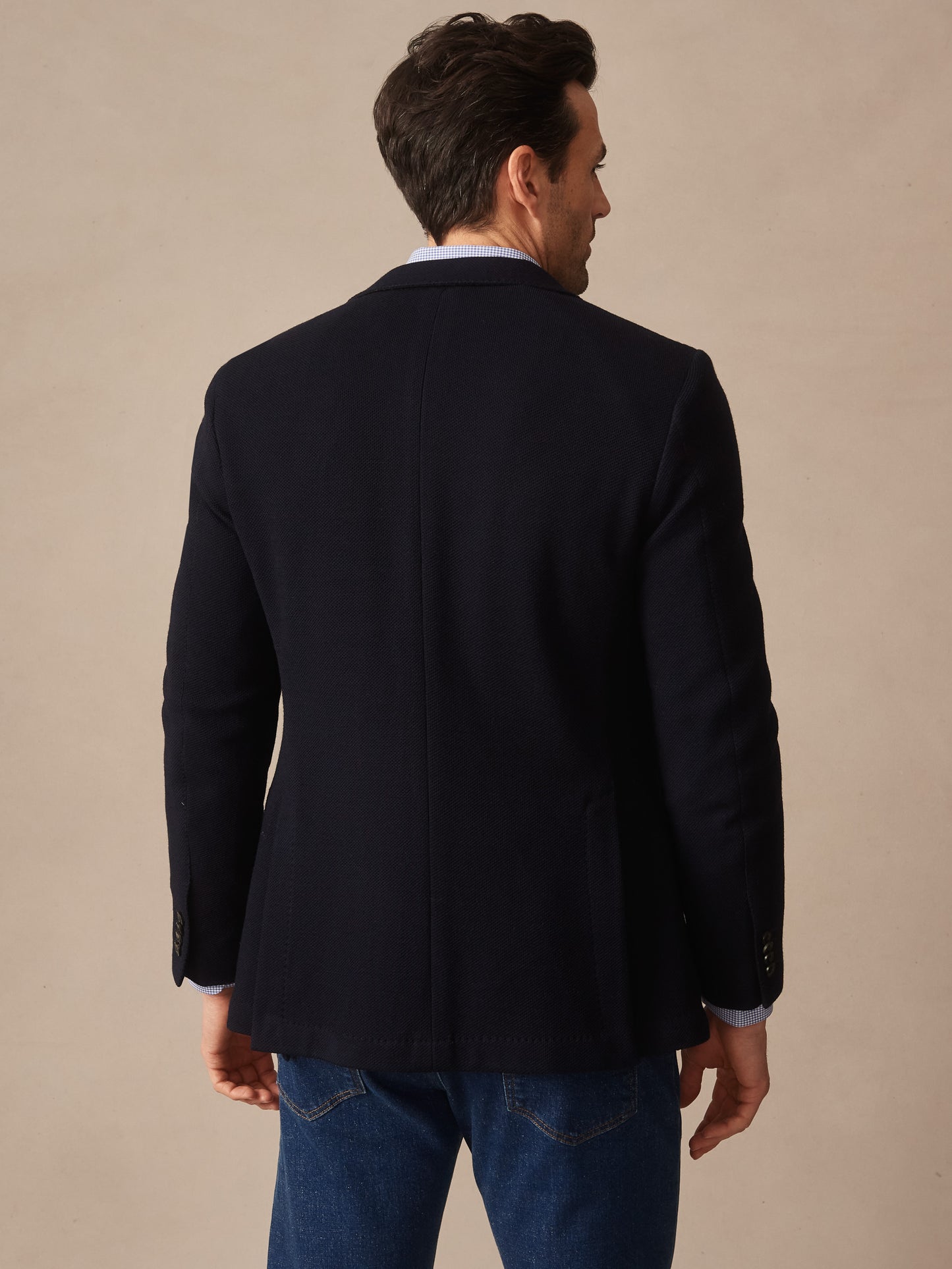 Man wearing a navy blue Canary Knit Blazer by J.McLaughlin, paired with jeans, showcasing effortlessly stylish, enduring designs in innovative fabrics for a legacy of timeless fashion.