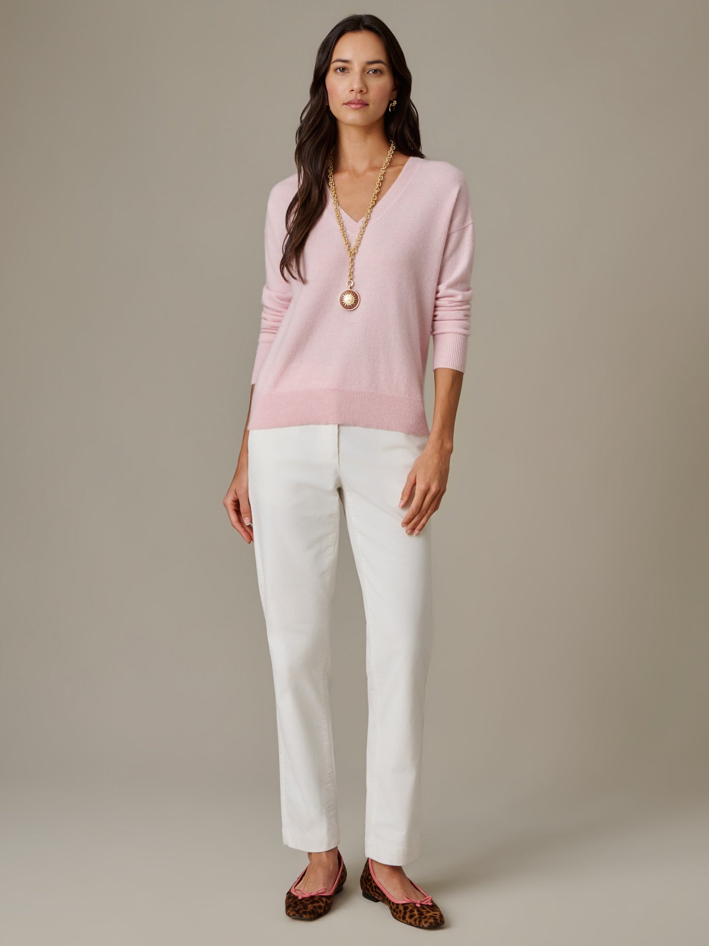 Woman wearing a soft pink Kerry Cashmere Sweater by J.McLaughlin paired with white pants and leopard print flats, showcasing effortlessly stylish, enduring designs.