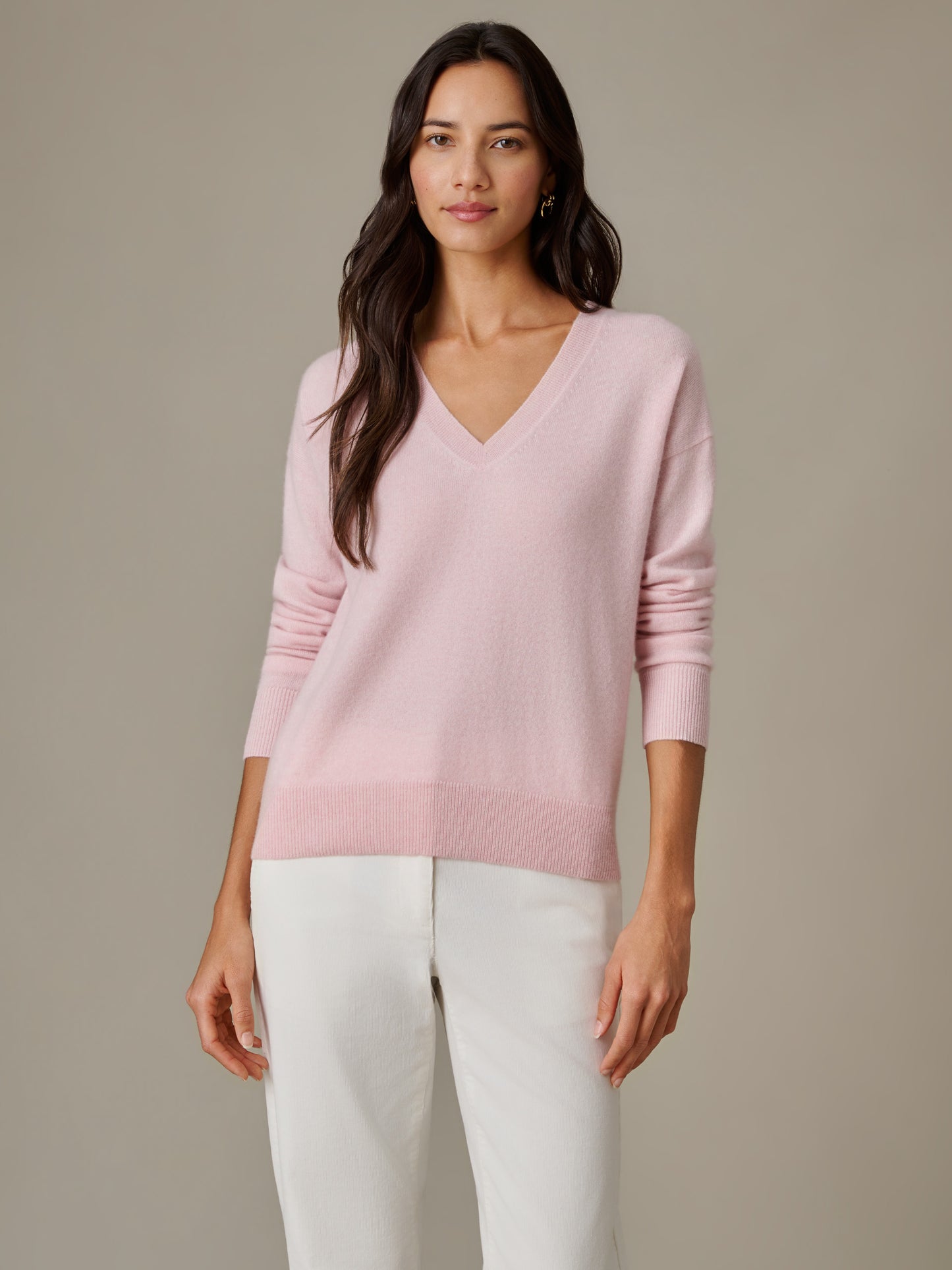 Woman wearing a soft pink Kerry Cashmere Sweater by J.McLaughlin, styled with white pants, showcasing an effortlessly stylish and timeless design perfect for enduring wardrobe appeal.