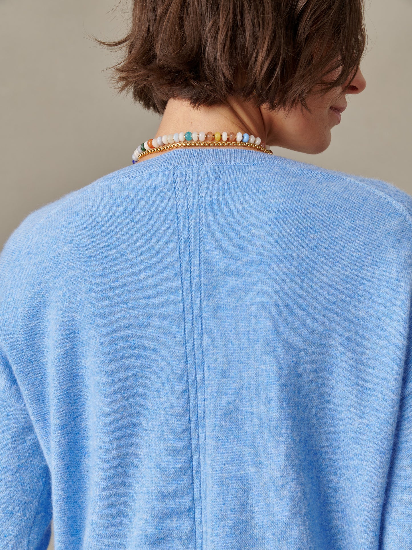 Back view of a person wearing a soft light blue Kerry Cashmere Sweater by J.McLaughlin paired with a colorful beaded necklace, showcasing timeless craftsmanship and enduring design.