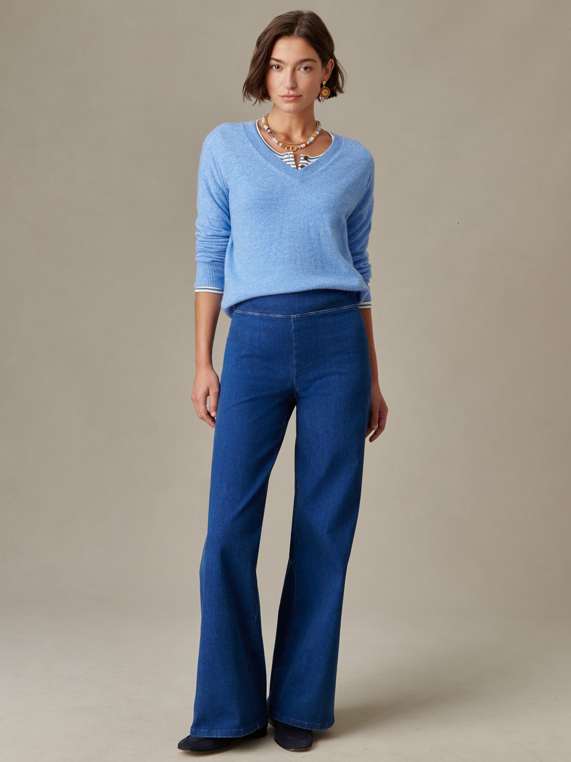 Woman wearing a light blue Kerry Cashmere Sweater by J.McLaughlin paired with dark blue wide-leg pants, styled with layered necklaces, showcasing effortlessly stylish and enduring design.