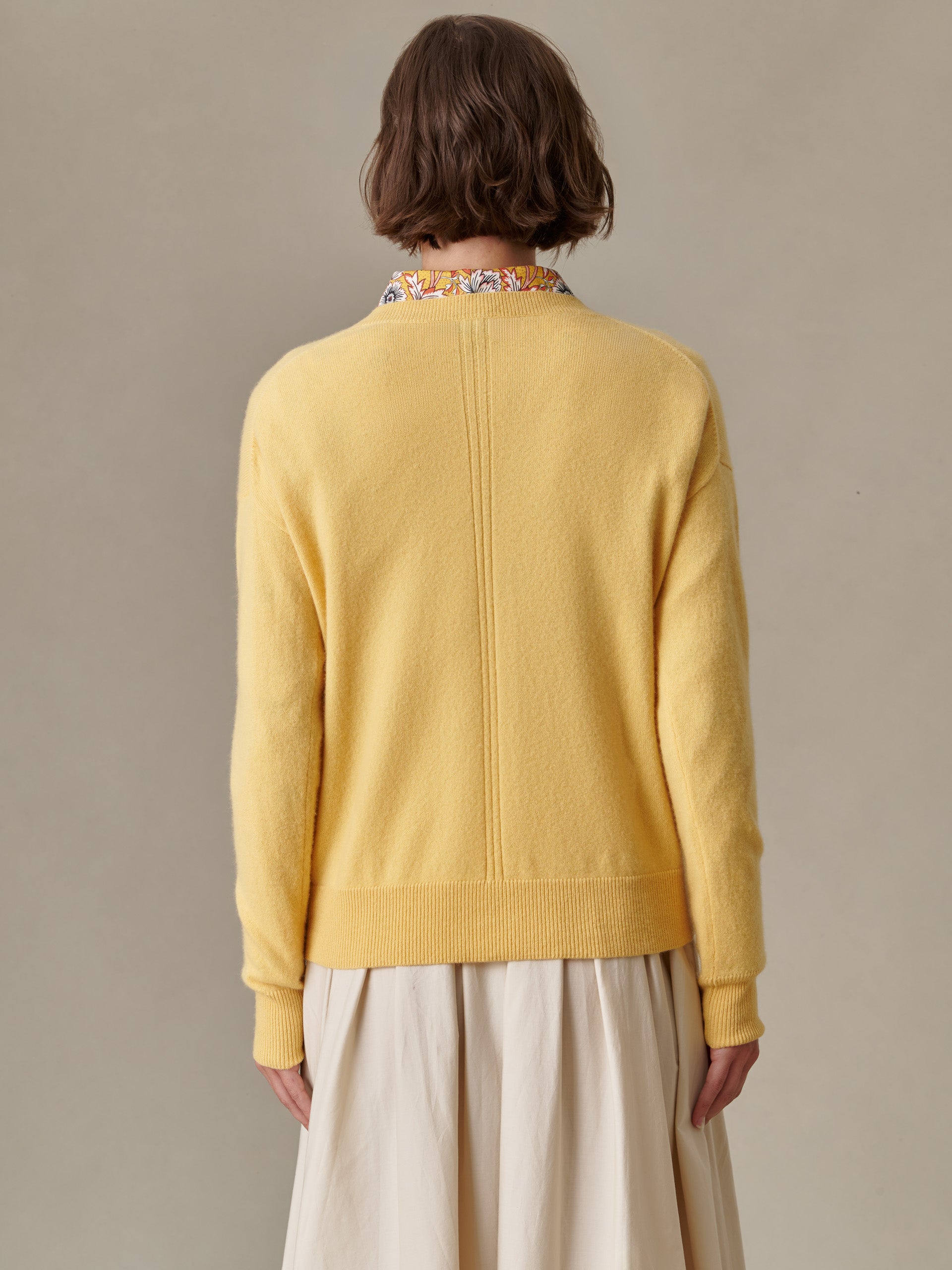 Back view of a person wearing a soft yellow Kerry Cashmere Sweater by J.McLaughlin, paired with a light floral collared shirt and beige skirt, showcasing thoughtful design and impeccable craftsmanship.