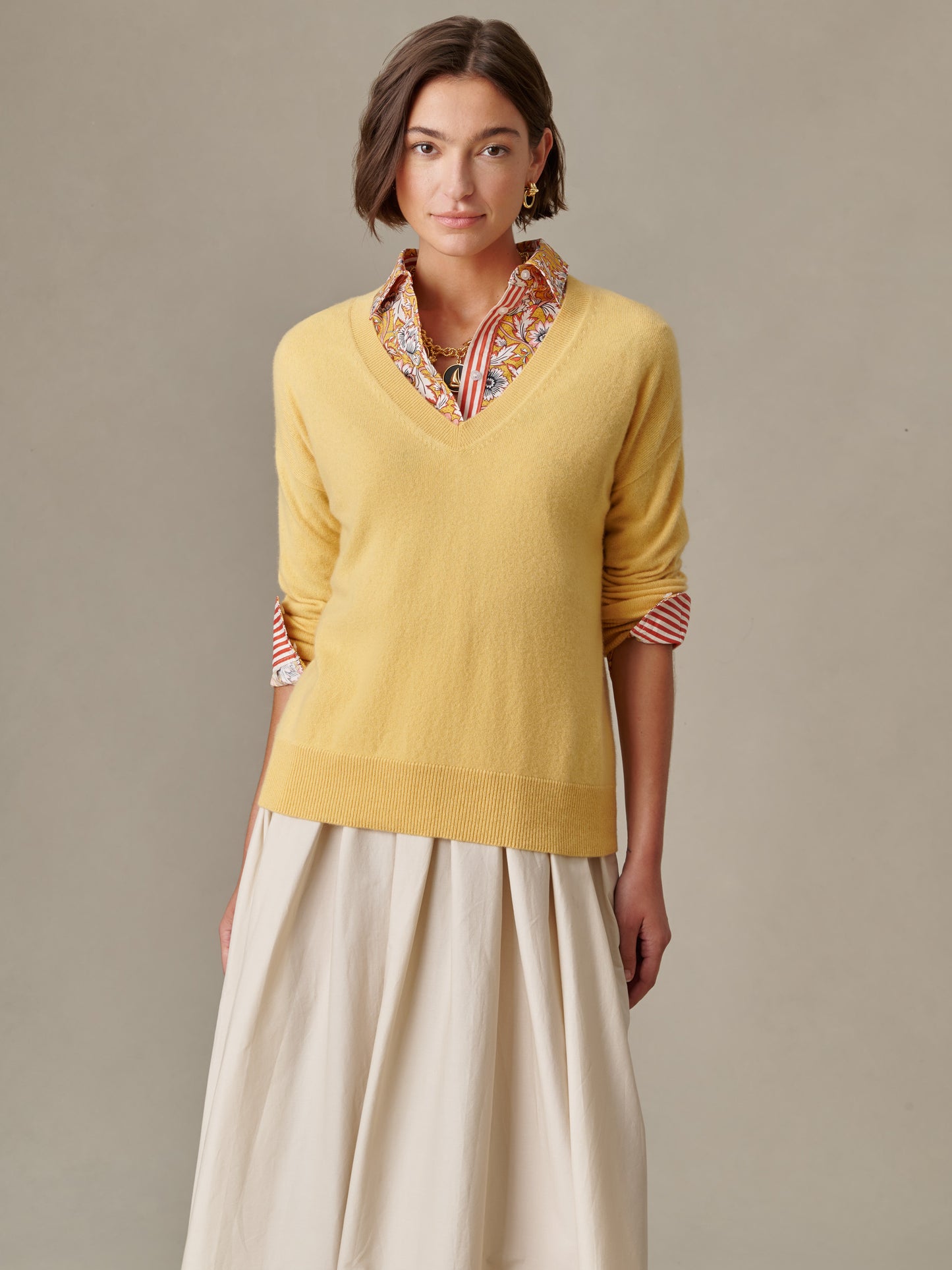 Woman wearing a soft yellow Kerry Cashmere Sweater from J.McLaughlin layered over a patterned blouse and flowing skirt, showcasing effortlessly stylish and enduring design.