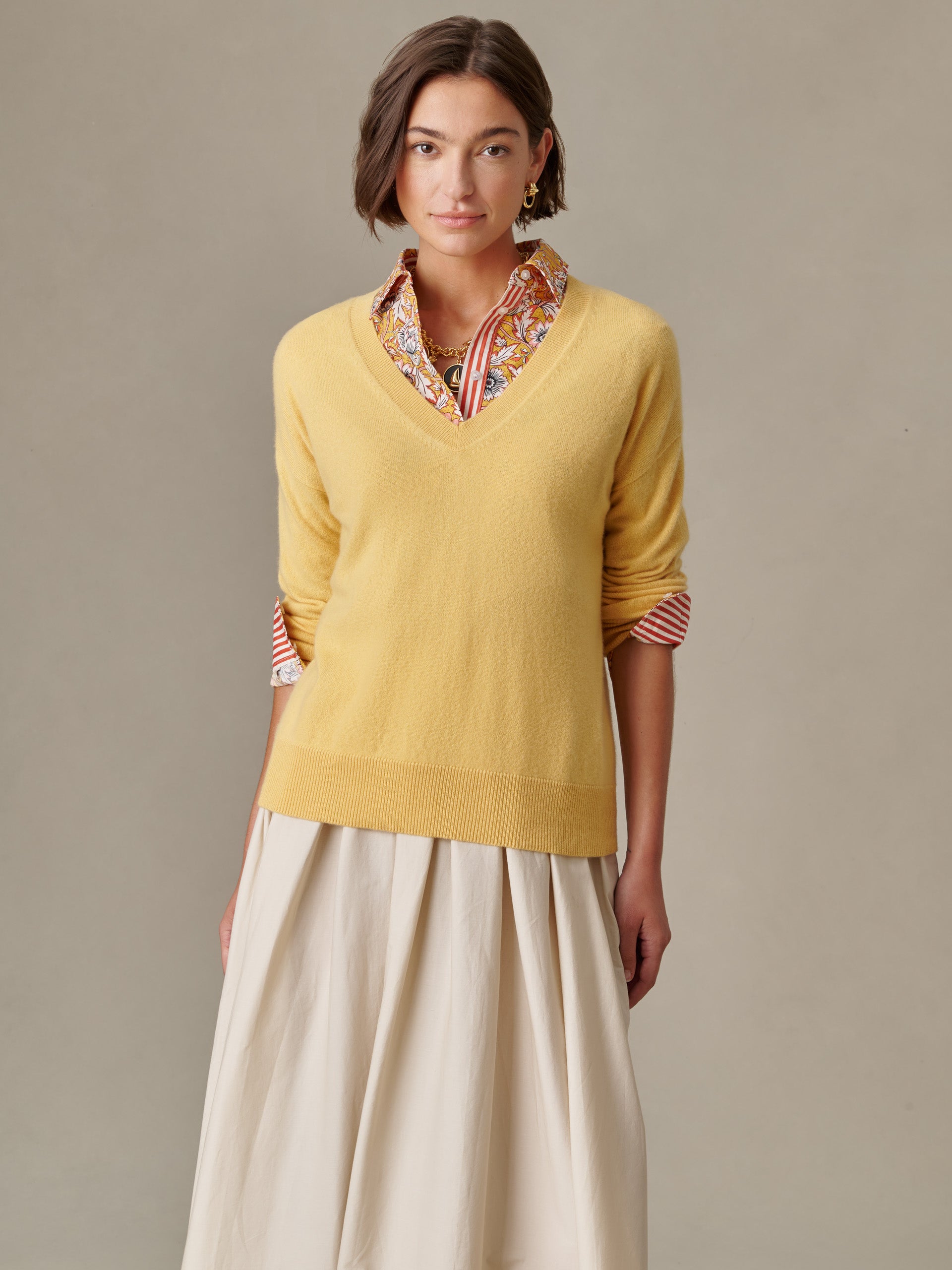 Woman wearing a soft yellow Kerry Cashmere Sweater from J.McLaughlin layered over a patterned blouse and flowing skirt, showcasing effortlessly stylish and enduring design.