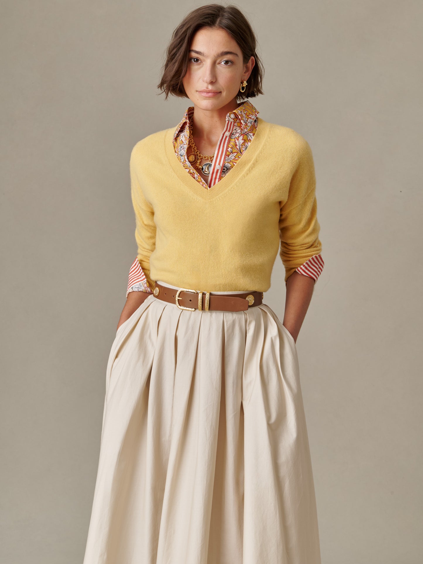 Woman wearing a yellow Kerry Cashmere Sweater by J.McLaughlin over a patterned blouse, paired with a beige skirt and brown belt, showcasing effortlessly stylish layering and timeless fashion.