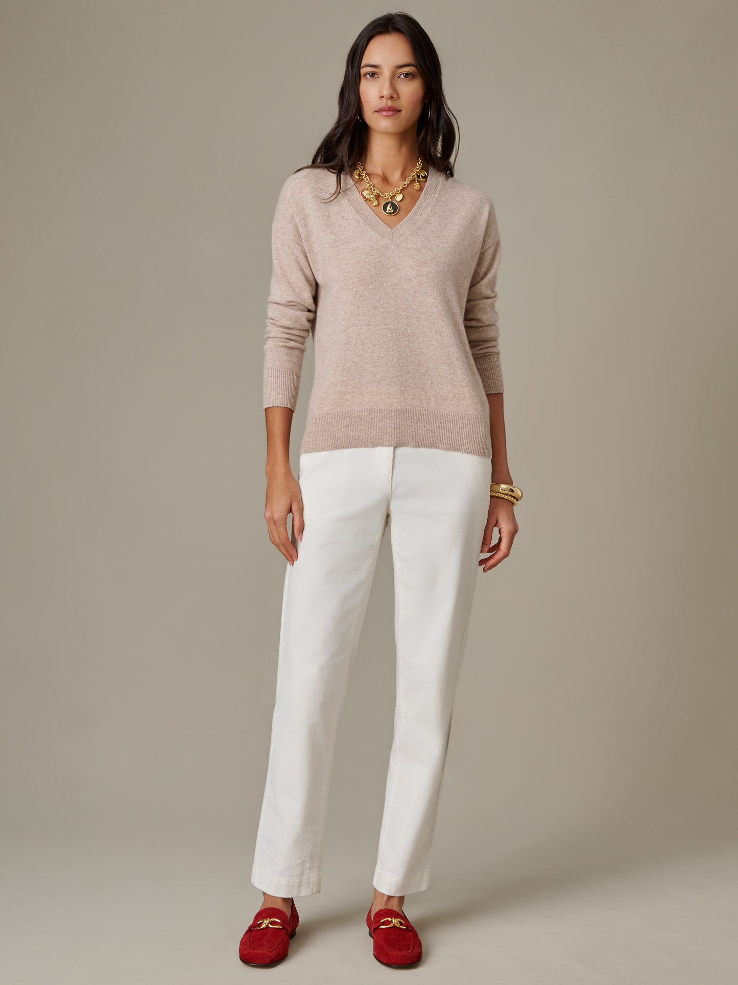 Woman wearing a Kerry Cashmere Sweater by J.McLaughlin in a soft beige color paired with white pants and red loafers, showcasing effortlessly stylish, enduring designs.