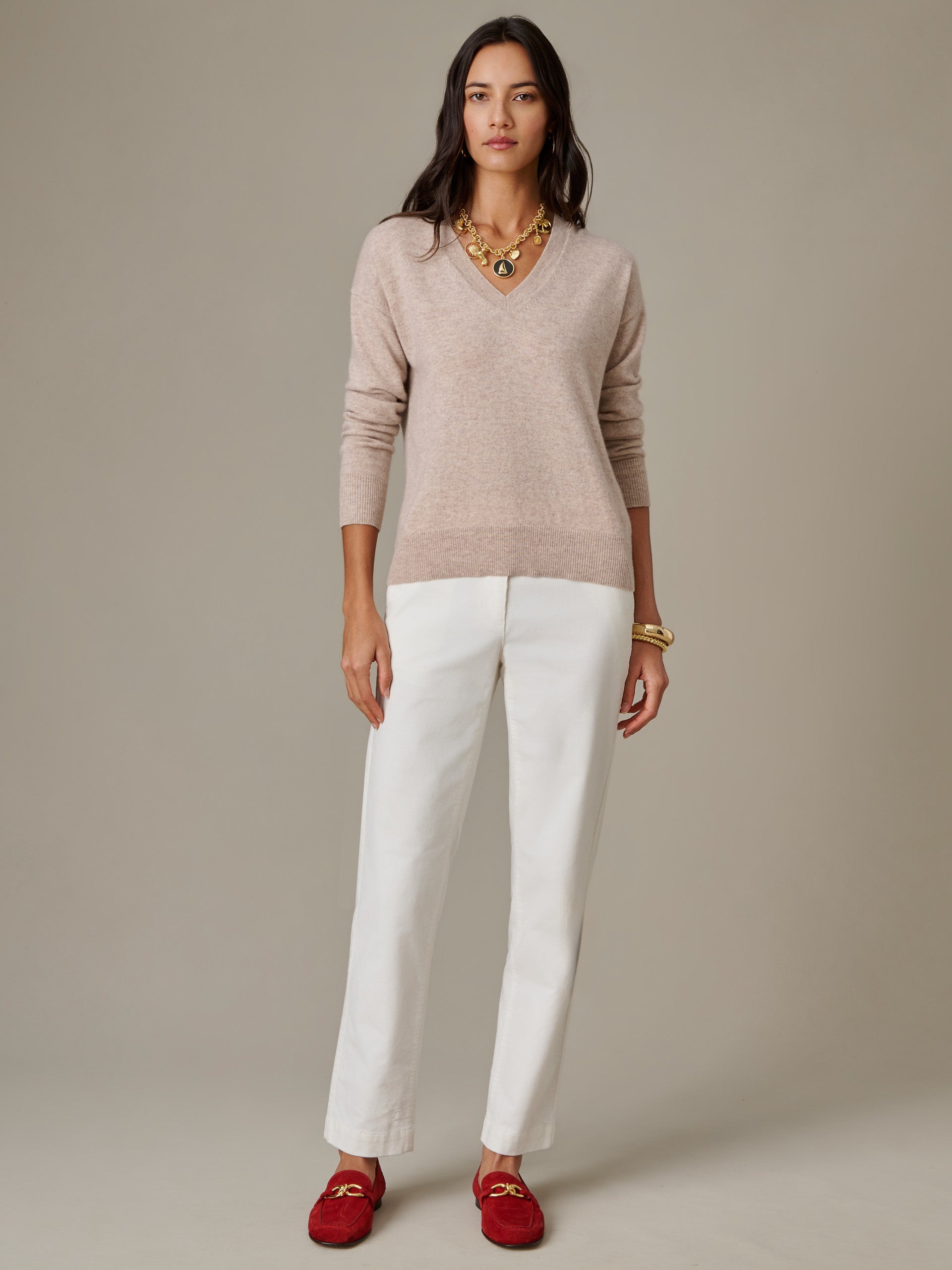Woman wearing a Kerry Cashmere Sweater by J.McLaughlin in a soft beige color paired with white pants and red loafers, showcasing effortlessly stylish, enduring designs.