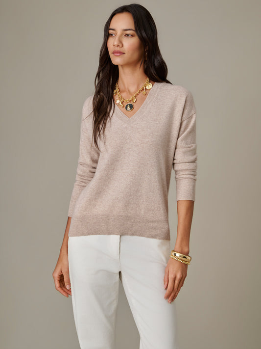Woman wearing a soft beige Kerry Cashmere Sweater by J.McLaughlin paired with white pants and gold jewelry, showcasing effortlessly stylish, enduring design.