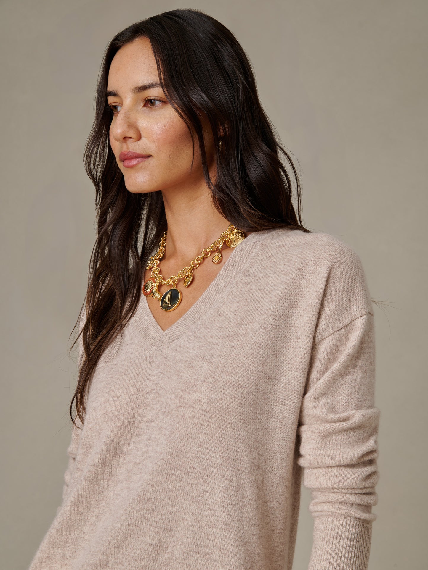 Woman wearing a soft beige Kerry Cashmere Sweater by J.McLaughlin paired with a gold charm necklace, showcasing effortlessly stylish and enduring design for timeless fashion.