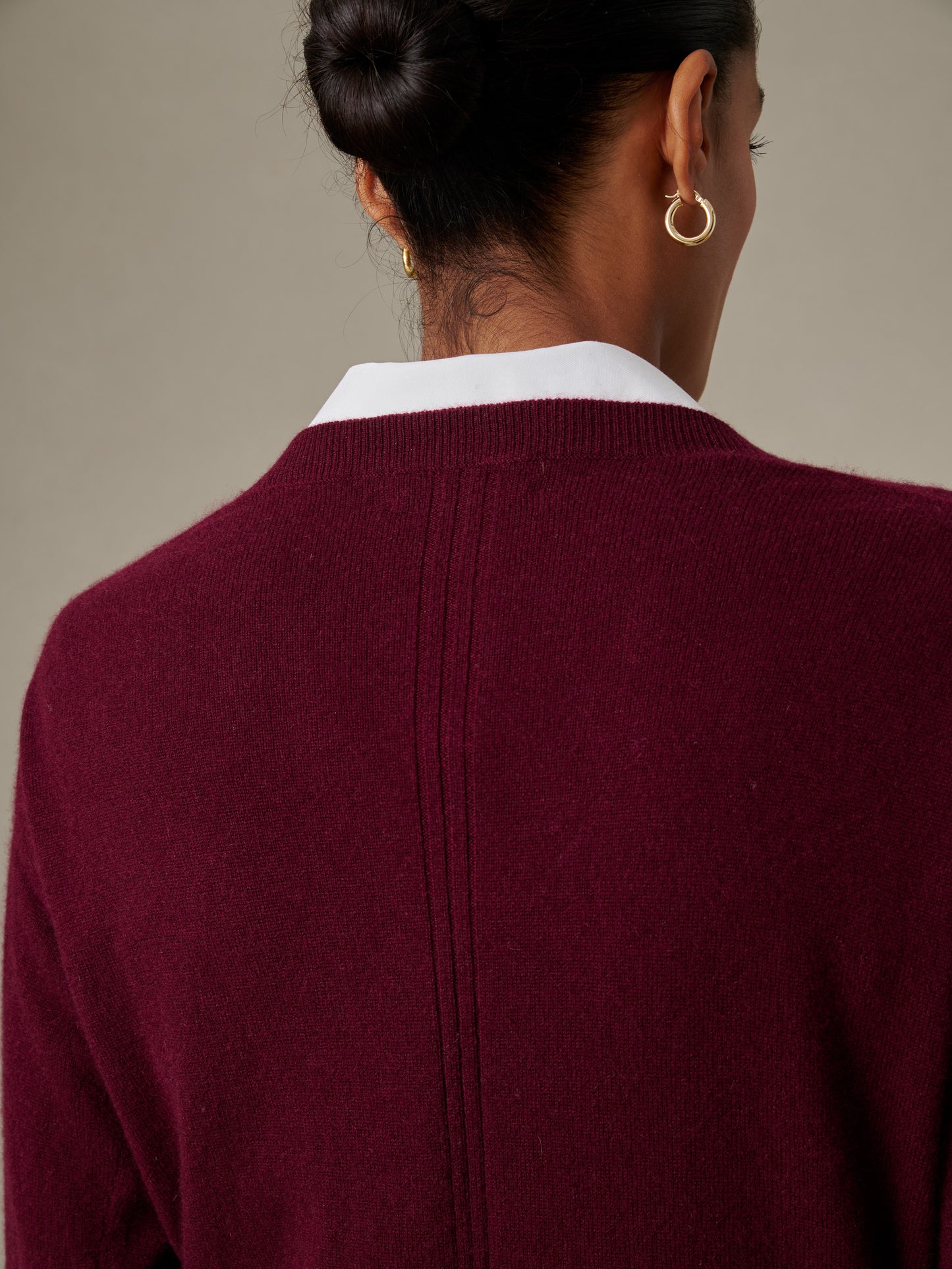 Close-up of a woman wearing a deep burgundy Kerry Cashmere Sweater by J.McLaughlin, showcasing its soft texture and classic design with gold hoop earrings and a white collar visible.