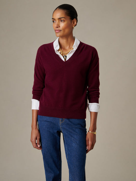Woman wearing a Kerry Cashmere Sweater in rich burgundy layered over a white shirt paired with blue jeans and gold jewelry, showcasing timeless, effortlessly stylish fashion by J.McLaughlin.