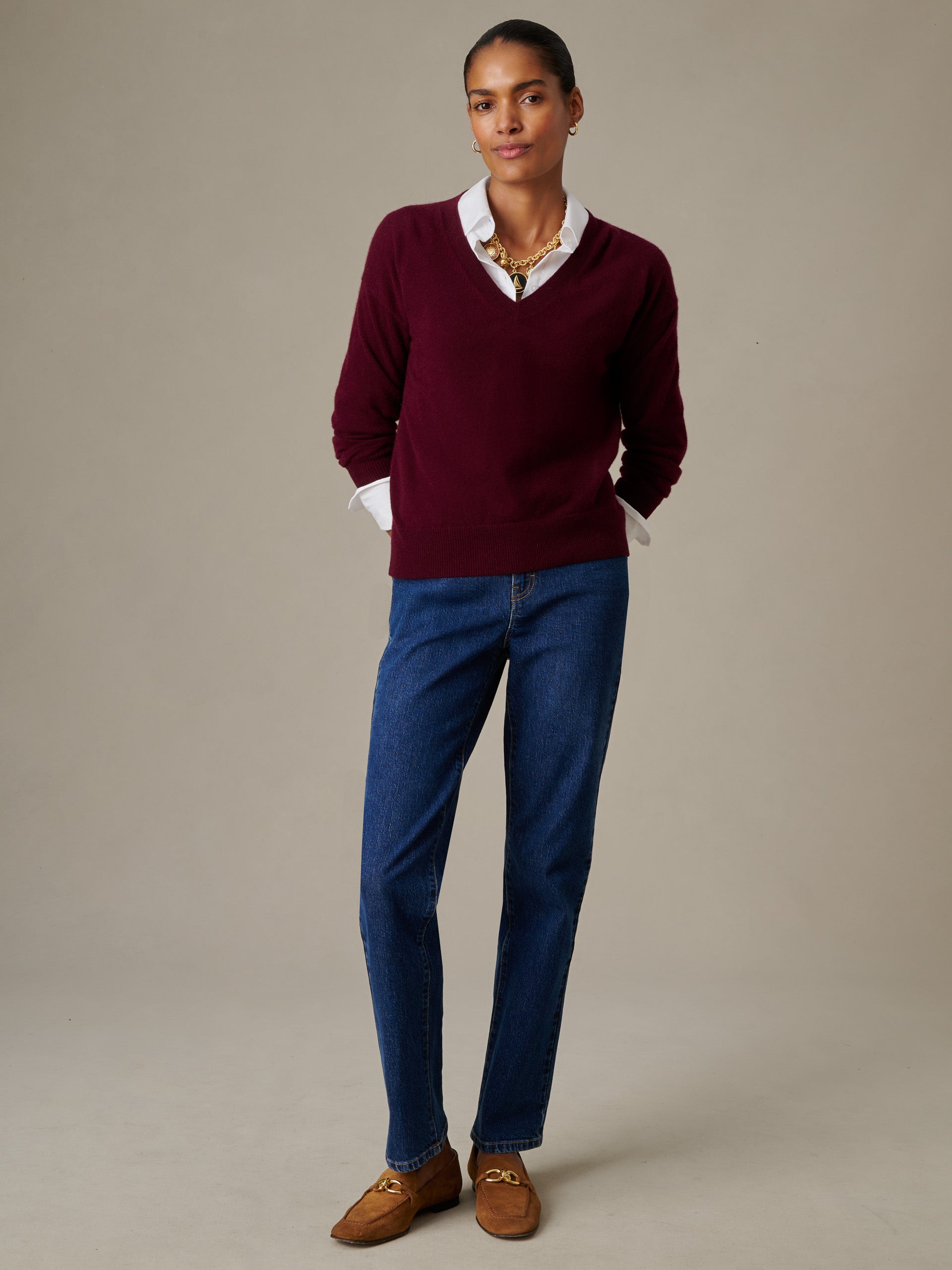 Woman wearing a deep burgundy Kerry Cashmere Sweater layered over a white collared shirt, paired with classic blue jeans and brown loafers, styled by J.McLaughlin.