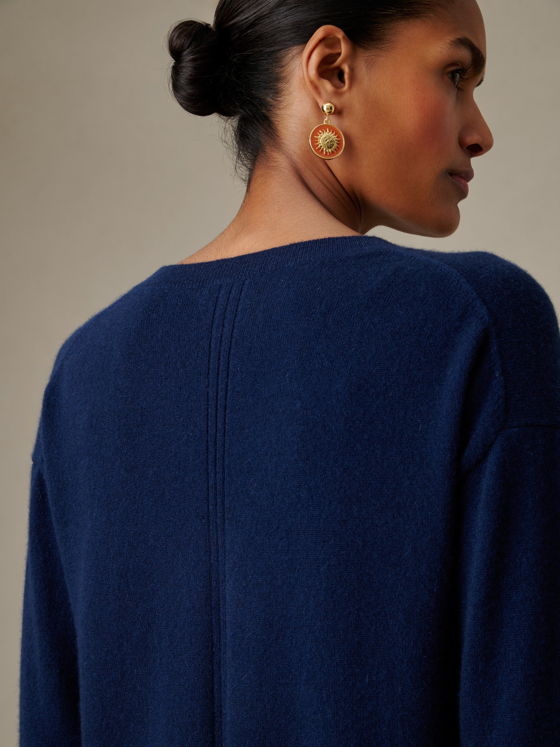 Woman wearing a navy Kerry Cashmere Sweater by J.McLaughlin with her hair in a bun and gold sunburst earrings, showcasing timeless style and enduring design.