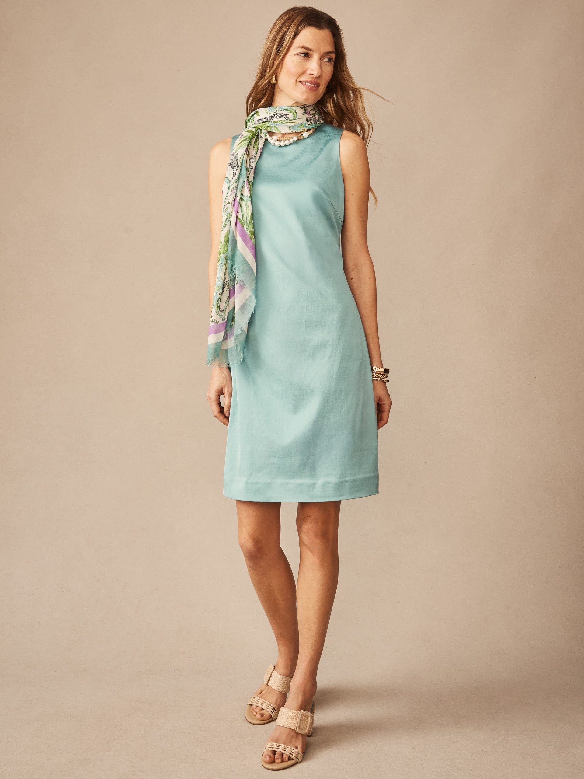 Woman wearing a seafoam sleeveless Kinsley Dress by J.McLaughlin paired with a colorful scarf and neutral sandals, showcasing effortlessly stylish, enduring designs.
