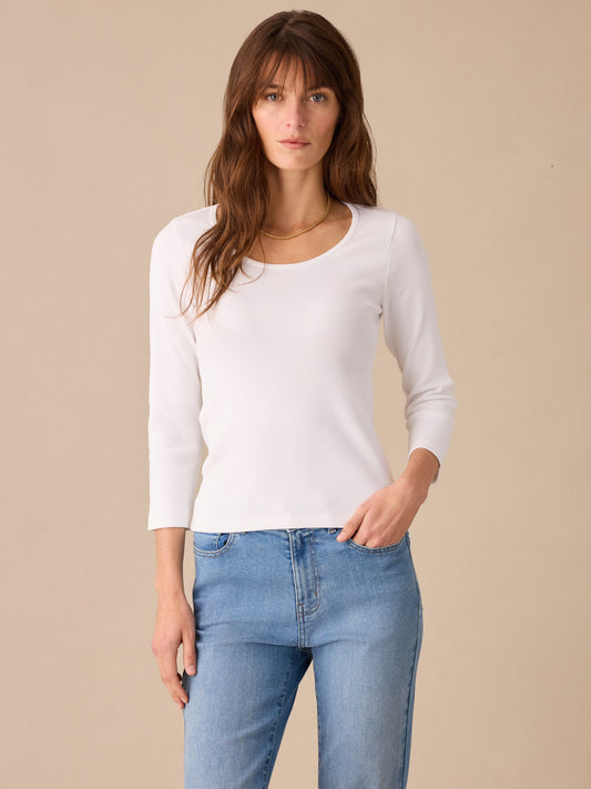 Woman wearing a white Kit Ribbed Tee by J.McLaughlin paired with light blue jeans, showcasing effortlessly stylish, enduring designs from a legacy of timeless fashion.