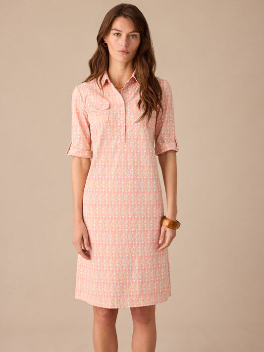 A model wearing the Lawrence Dress in Neo Jewel Ikat by J.McLaughlin, featuring a soft coral and white pattern with a classic shirt collar and rolled sleeves, showcasing effortlessly stylish, enduring designs with innovative fabrics. A destination for defining style. Life, Well-Lived.