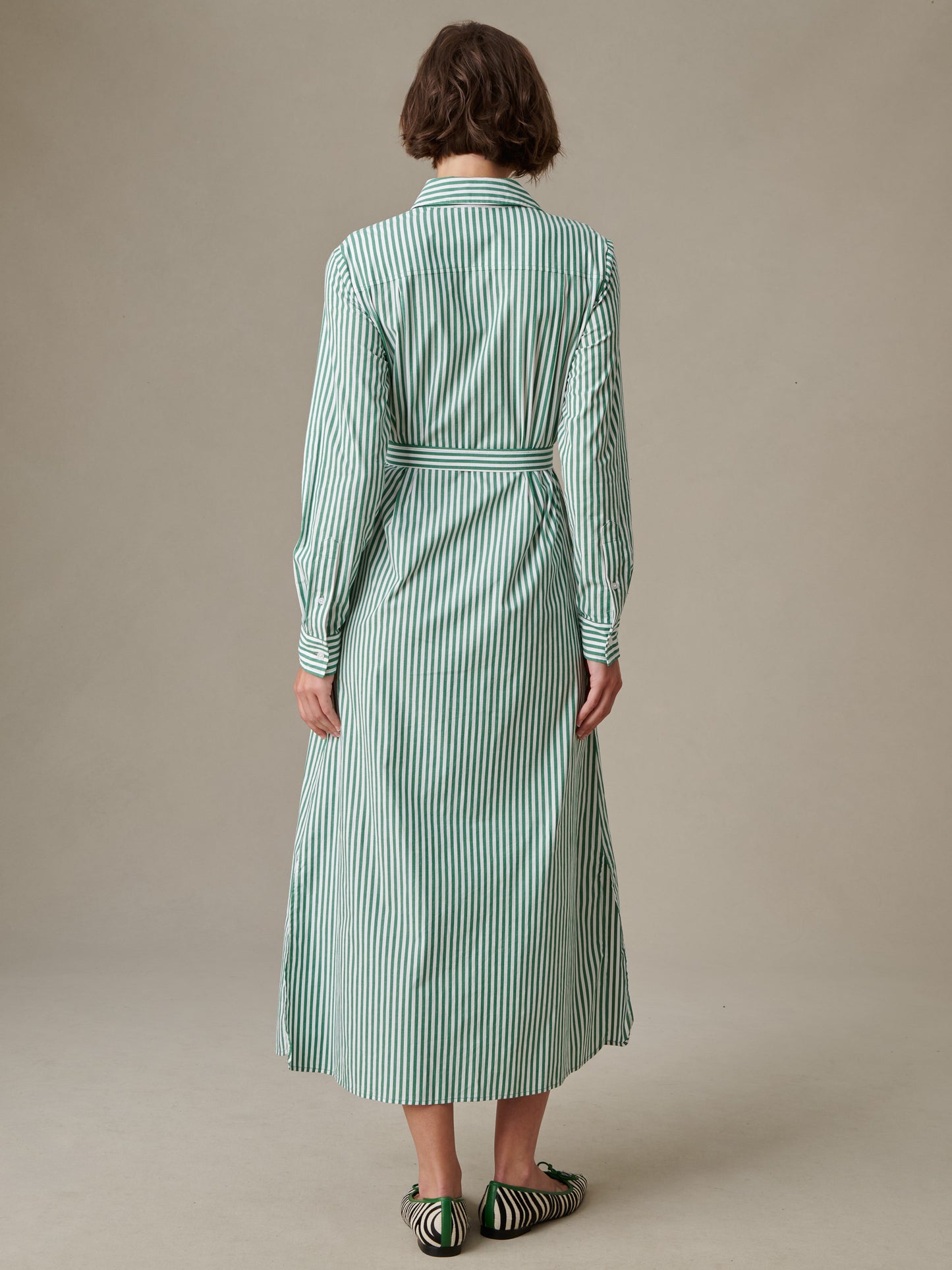 Back view of a woman wearing the Leighton Dress in Stripe by J.McLaughlin, featuring vertical green and white stripes, a belted waist, and long sleeves for an effortlessly stylish look.
