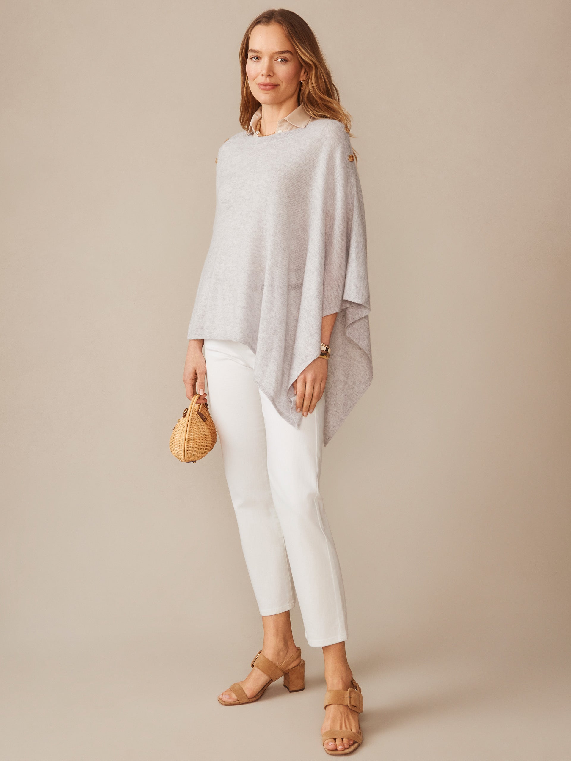A woman models the Leila Cashmere Poncho in light grey by J.McLaughlin, paired with white pants, tan sandals, and a small woven handbag, embodying effortlessly stylish, enduring designs with a legacy of timeless fashion at a destination for defining style. Life, Well-Lived.