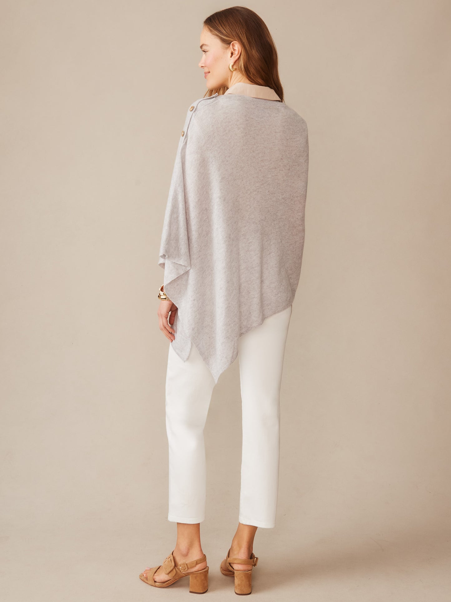 Woman wearing a light grey Leila Cashmere Poncho by J.McLaughlin, styled with white pants and neutral sandals, showcasing effortlessly stylish, enduring designs in innovative fabrics.