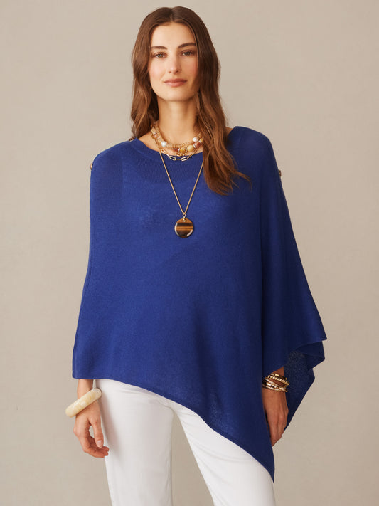 A woman wears the Leila Cashmere Poncho in rich navy blue by J.McLaughlin, showcasing effortlessly stylish layering with enduring designs and a legacy of timeless fashion.