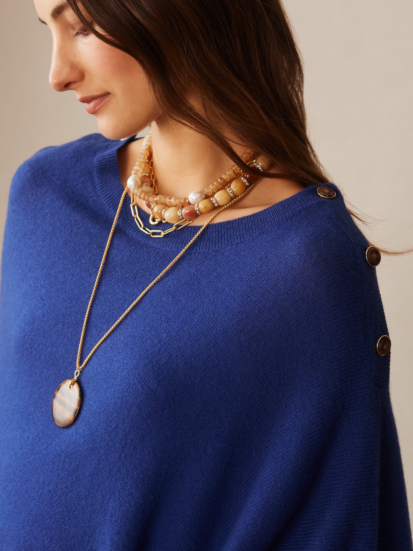 A woman wearing a nautical navy Leila Cashmere Poncho by J.McLaughlin, styled with layered necklaces, showcasing effortlessly stylish, enduring designs and a legacy of timeless fashion.