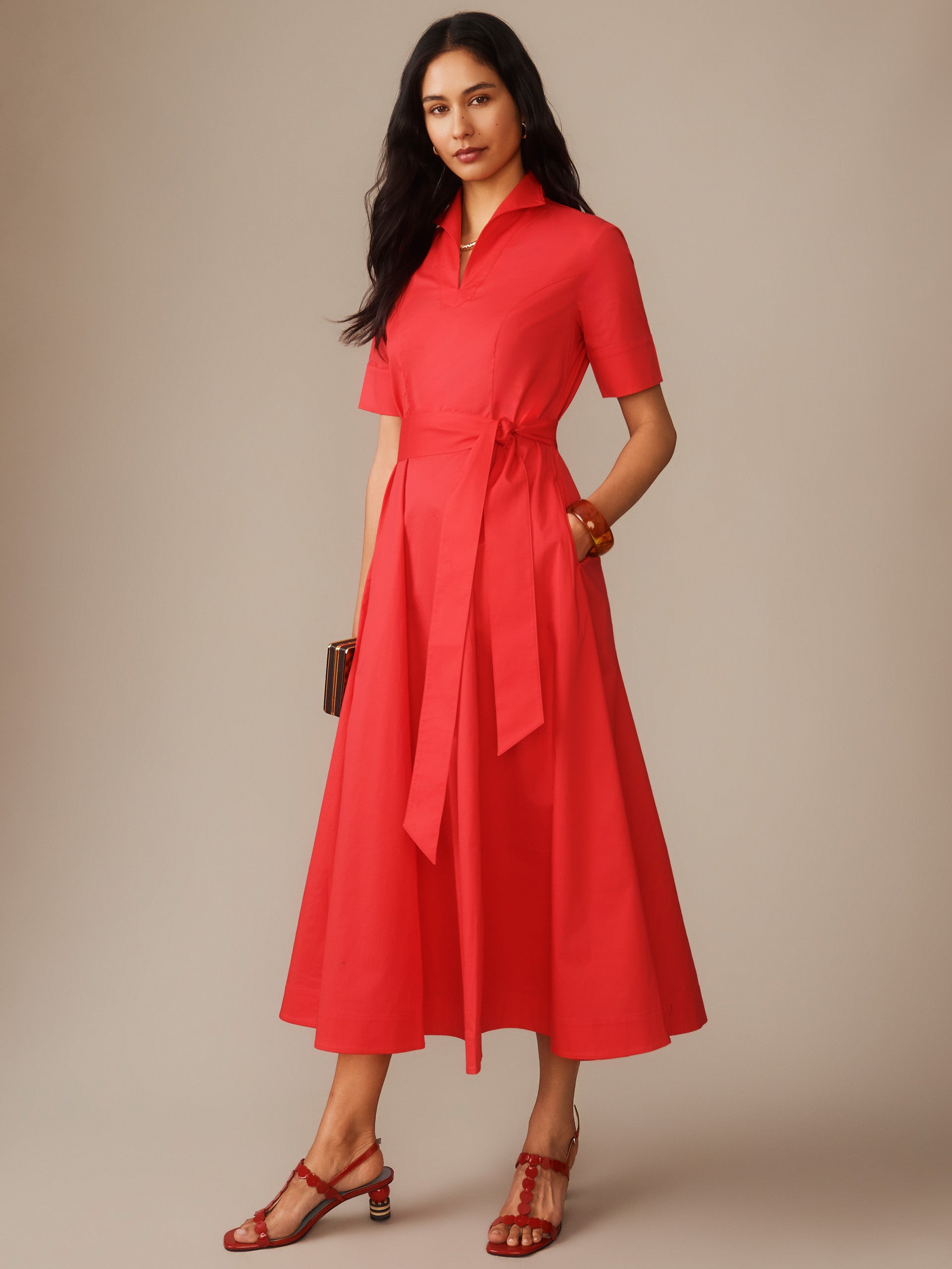 Woman wearing a vibrant red Lily Dress by J.McLaughlin featuring a collared neckline, short sleeves, a tied waist, and a flowing skirt, embodying effortlessly stylish, enduring designs.