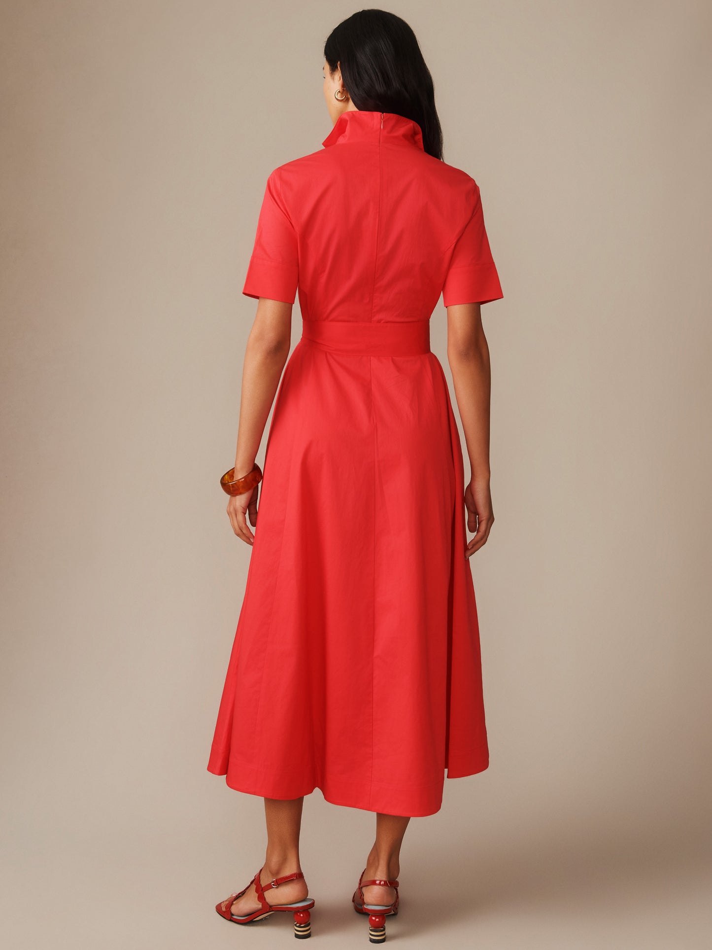 Woman wearing a vibrant red Lily Dress by J.McLaughlin, featuring a high collar, short sleeves, and a belted waist, embodying effortlessly stylish, enduring designs.