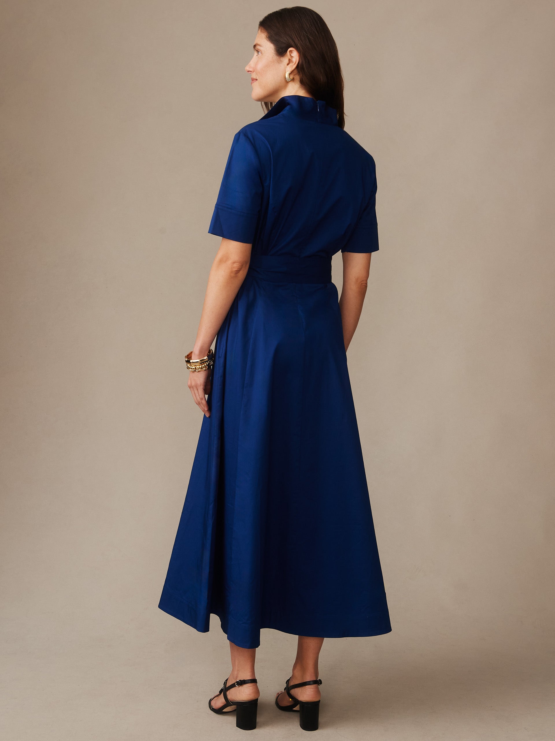 Woman wearing a navy blue Lily Dress by J.McLaughlin, featuring short sleeves and a midi length, styled with black heeled sandals and gold bracelets.
