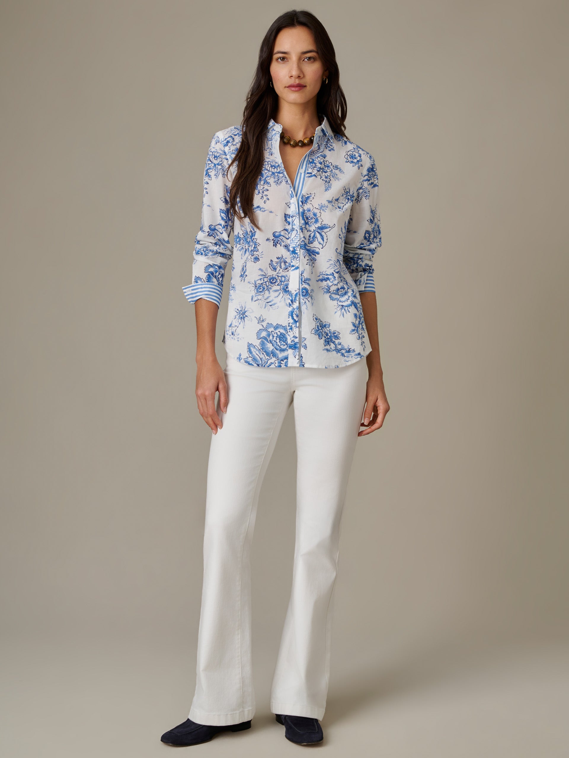 Woman wearing a Lois Shirt in Antique Toile Stripe by J.McLaughlin, featuring classic blue floral patterns on white fabric paired with white pants, embodying enduring style and craftsmanship.