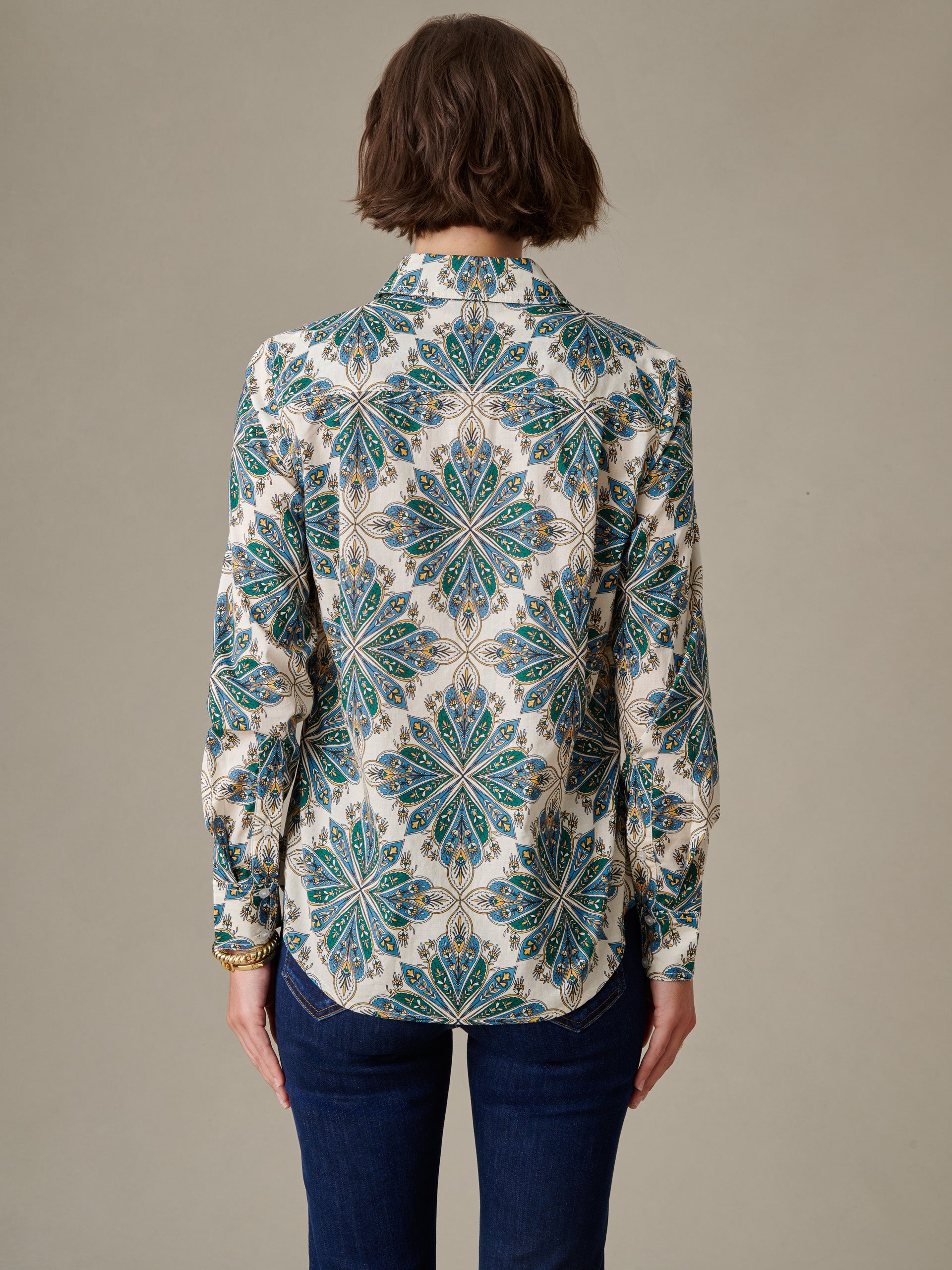 Woman wearing a Lois Shirt in Neo Radiant Stripe by J.McLaughlin, featuring a classic, intricate blue and green patterned blouse paired with dark jeans, embodying timeless style.