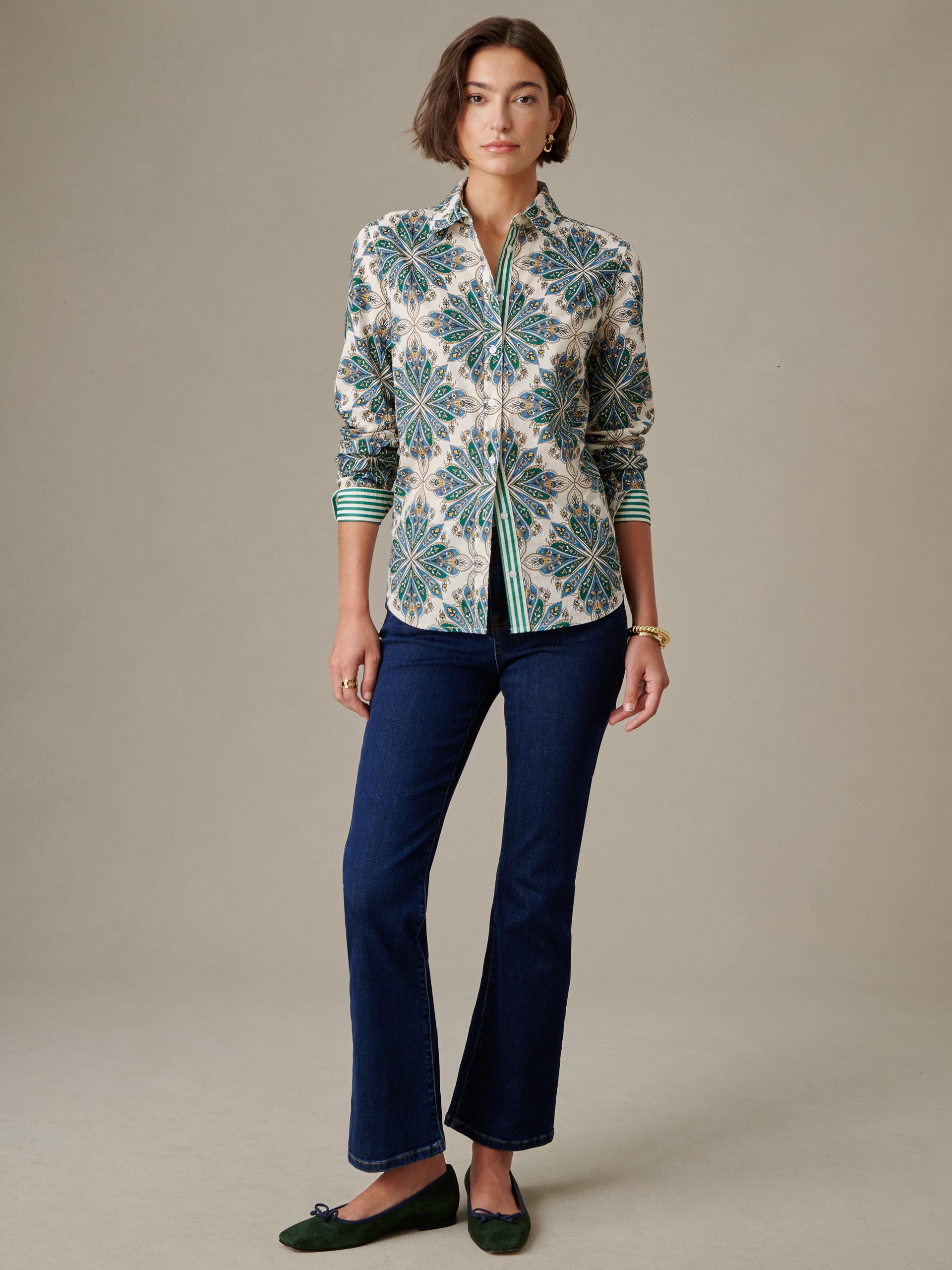 Woman wearing the Lois Shirt in Neo Radiant Stripe by J.McLaughlin, featuring an intricate floral pattern with green accents, paired with dark jeans and green flats.