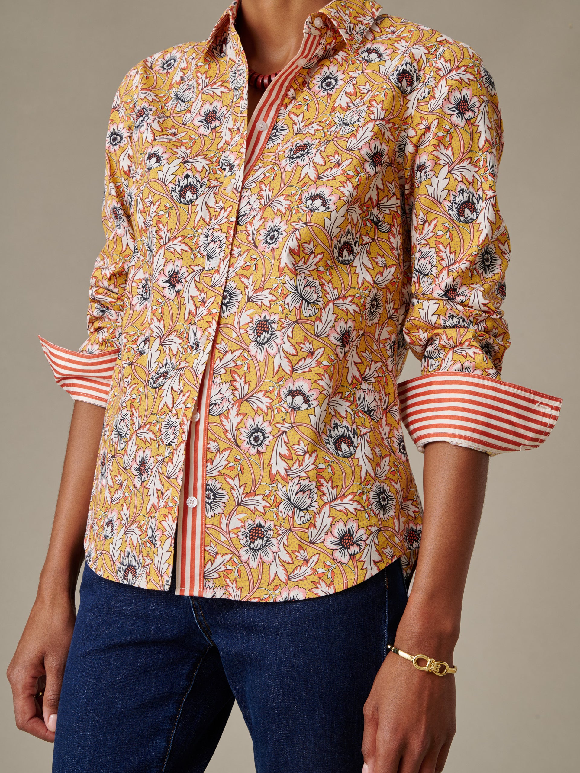 Close-up of a person wearing the Lois Shirt in Belle Epoque Bloom Stripe by J.McLaughlin, featuring a floral pattern with contrasting striped cuffs and placket, paired with dark jeans and a gold bracelet.