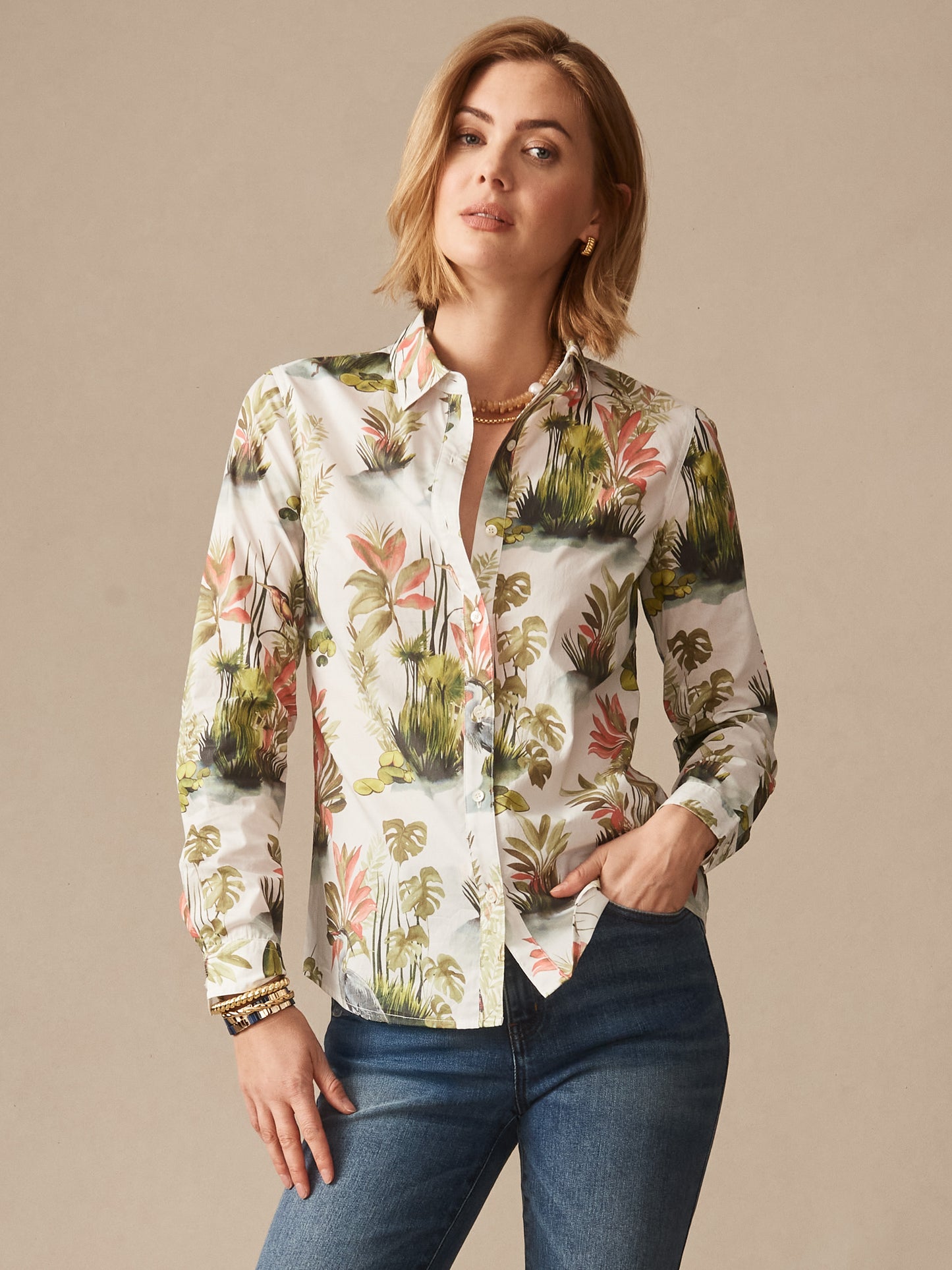Woman wearing a Lois Shirt in Tidal Palms by J.McLaughlin featuring a tropical print in green and coral tones paired with jeans, showcasing effortlessly stylish, enduring designs and innovative fabrics.
