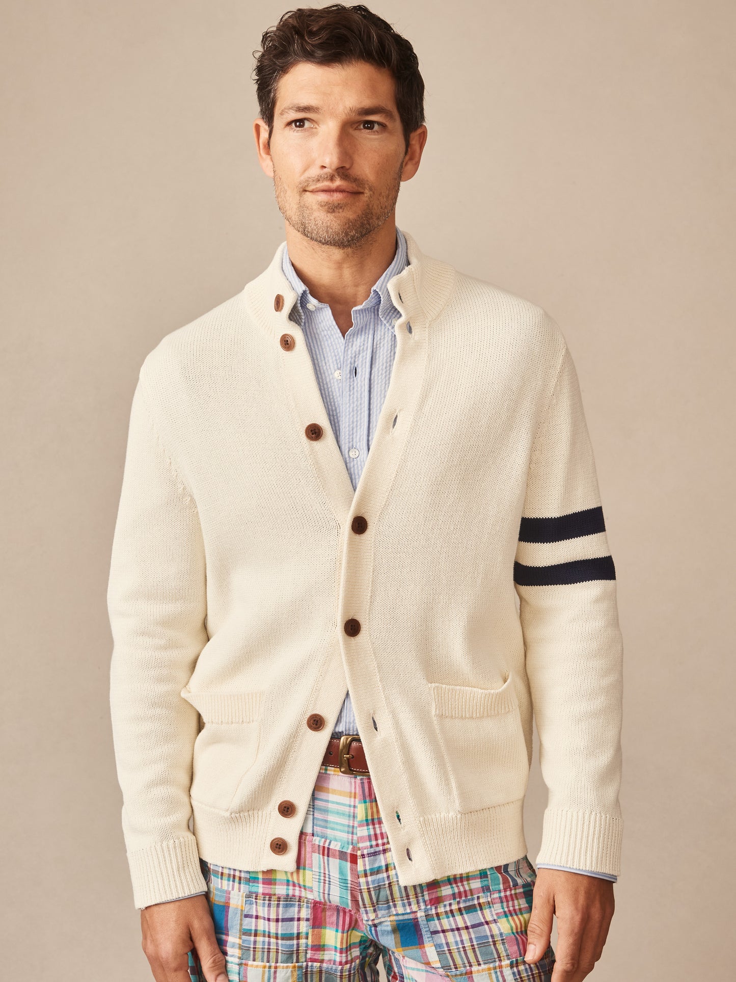 Man wearing an off-white Lowell Sweater by J.McLaughlin with navy stripes on the sleeve, brown buttons, and a light blue shirt underneath.