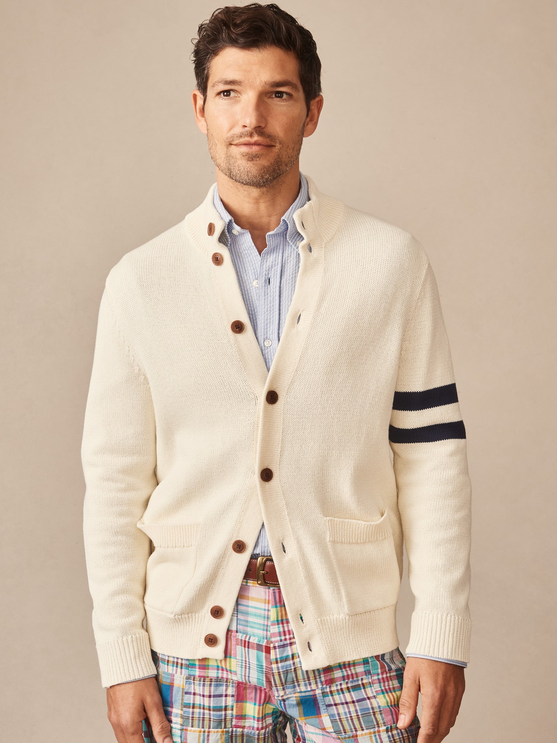 Man wearing an off-white Lowell Sweater by J.McLaughlin with navy stripes on the sleeve, brown buttons, and a light blue shirt underneath.