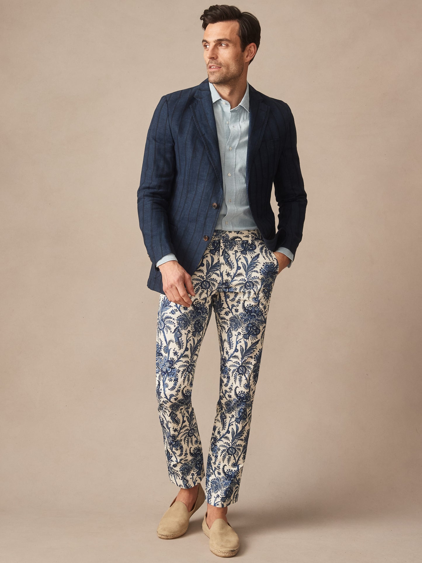 A stylish man wearing J.McLaughlin's Madison Fancy Pants in Heirloom Paisley paired with a navy blazer and light blue shirt, showcasing effortlessly stylish, enduring designs.