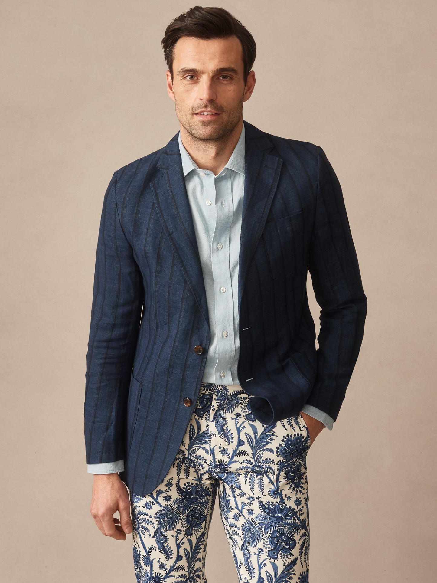 Man wearing a Brera Linen Silk Sport Coat in Stripe by J.McLaughlin, paired with a light blue shirt and patterned pants, showcasing effortlessly stylish, enduring designs with innovative fabrics, embodying a legacy of timeless fashion. A destination for defining style. Life, Well-Lived.