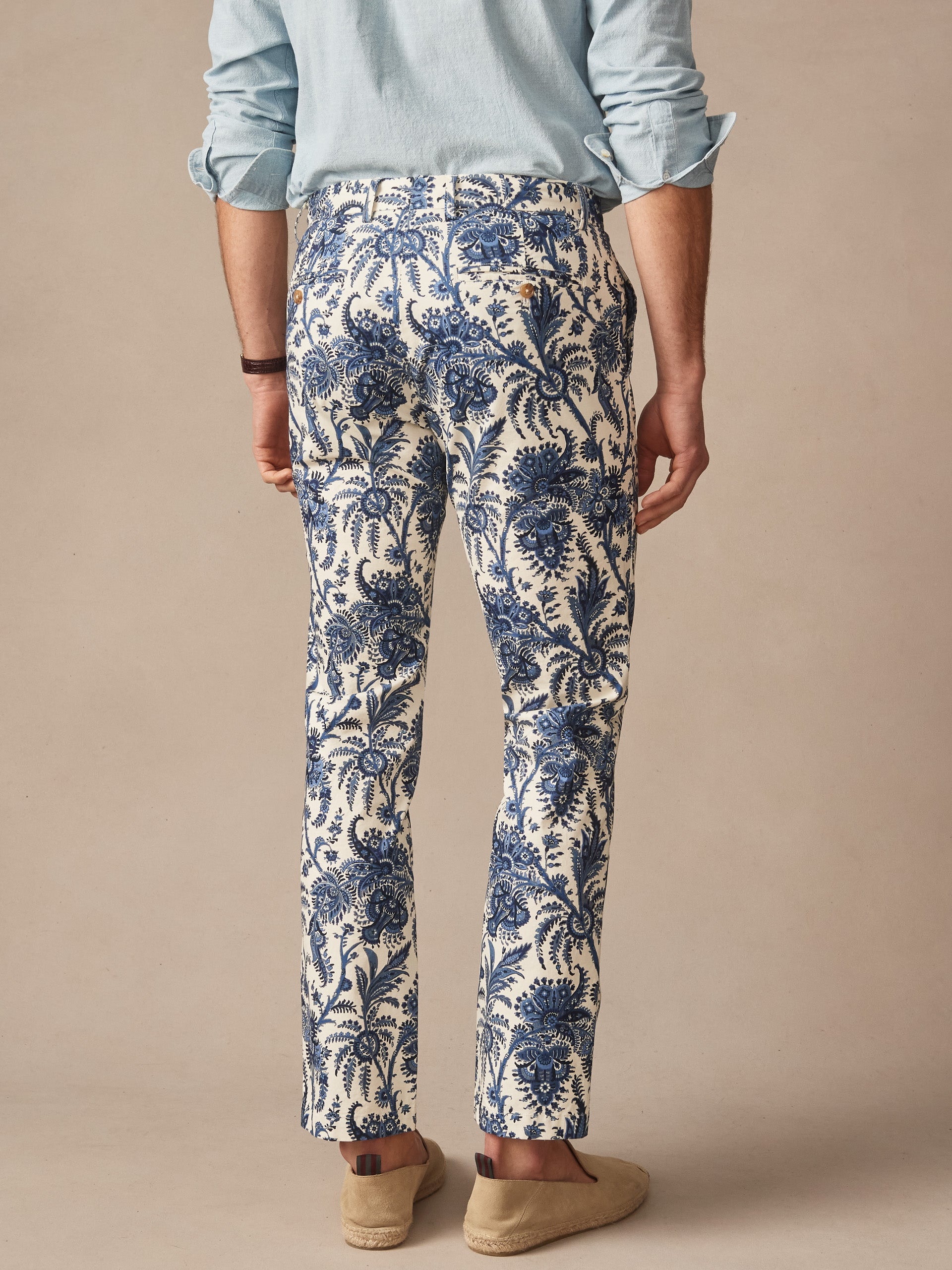 Man wearing Madison Fancy Pants in Heirloom Paisley by J.McLaughlin, featuring an intricate cream and navy pattern, paired with a light blue shirt and casual slip-on shoes, showcasing effortlessly stylish design and enduring craftsmanship. A destination for defining style. Life, Well-Lived.