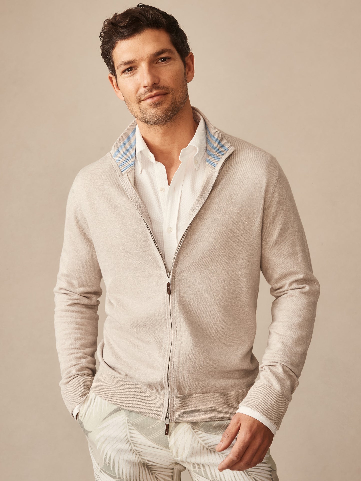 Man wearing a neutral-toned Orwell Sweater by J.McLaughlin, featuring a zip-up front and subtle striped collar detail, embodying effortlessly stylish, enduring designs for a life well-lived.