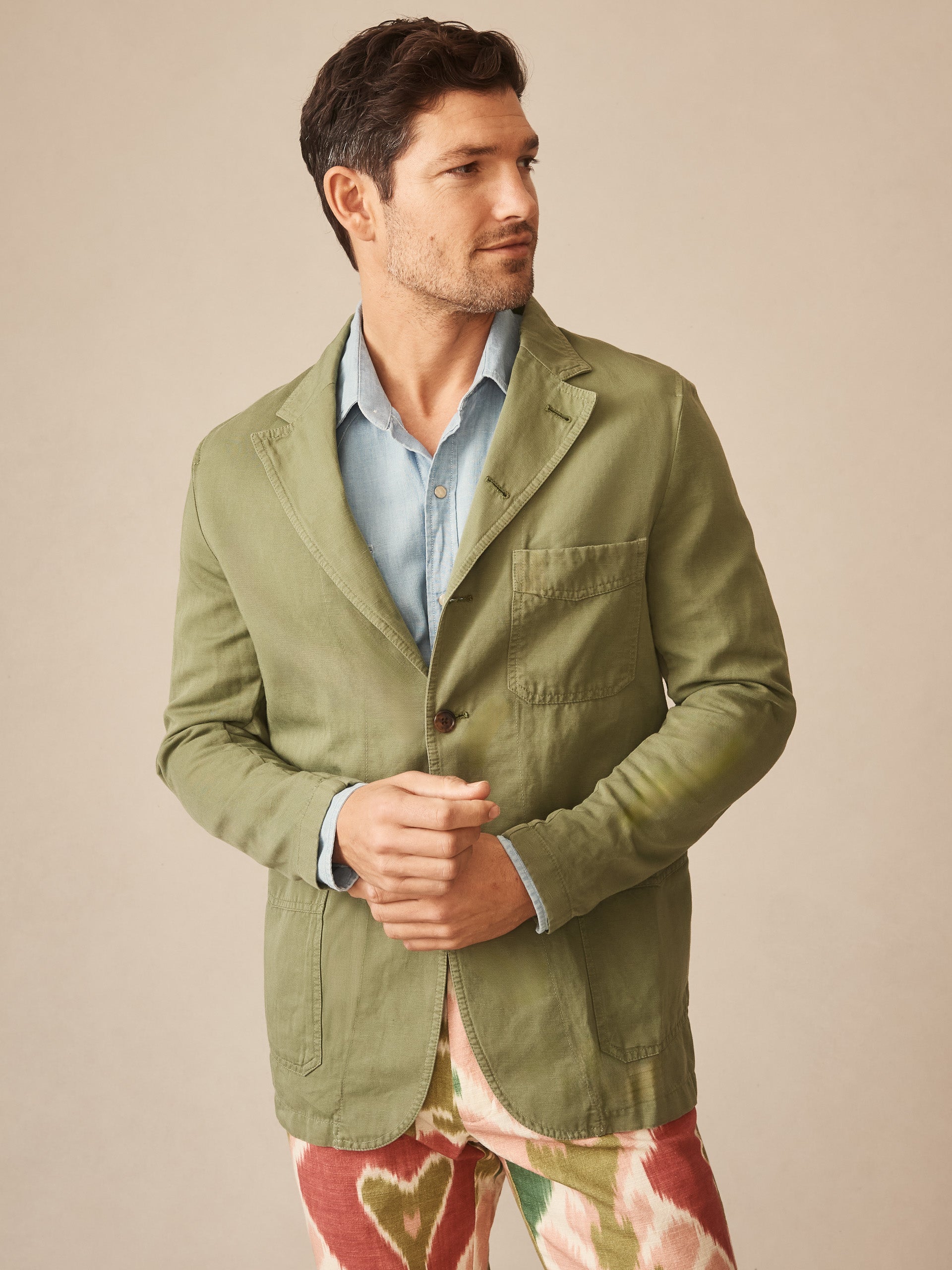 Man wearing an olive green Charlestown Jacket by J.McLaughlin over a light blue shirt, showcasing effortlessly stylish layering and enduring designs, a destination for defining style. Life, Well-Lived.