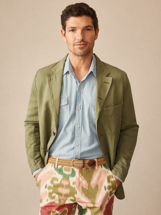 Man wearing a J.McLaughlin Charlestown Jacket in sage green over a light blue shirt paired with patterned pants and a woven belt, showcasing effortlessly stylish, enduring designs and innovative fabrics. A destination for defining style. Life, Well-Lived.