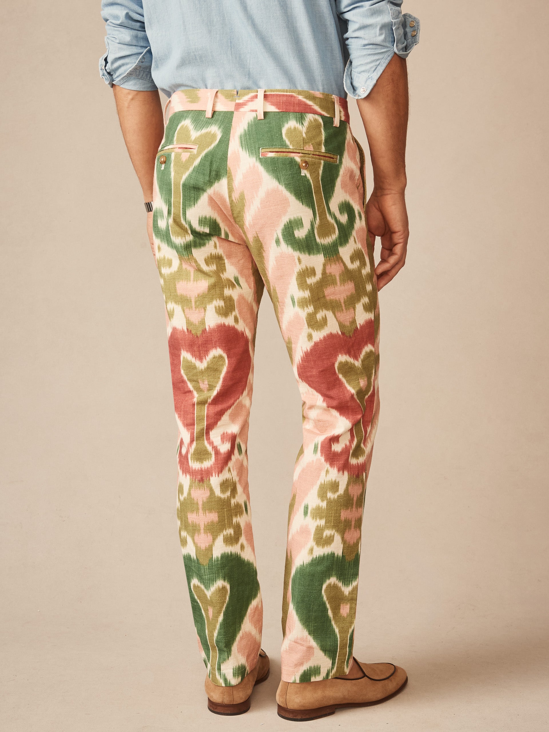 Man wearing Madison Fancy Pants in Ikat by J.McLaughlin, featuring a colorful green, cream, and red pattern, paired with casual suede shoes and a light blue rolled-up shirt. Effortlessly stylish pants crafted with innovative fabrics, reflecting enduring designs from a legacy of timeless fashion. A destination for defining style. Life, Well-Lived.