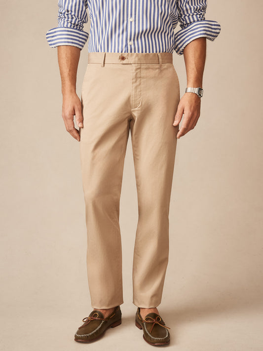 Man wearing beige Madison Pants by J.McLaughlin paired with a blue and white striped shirt and brown loafers, showcasing effortlessly stylish, enduring designs.